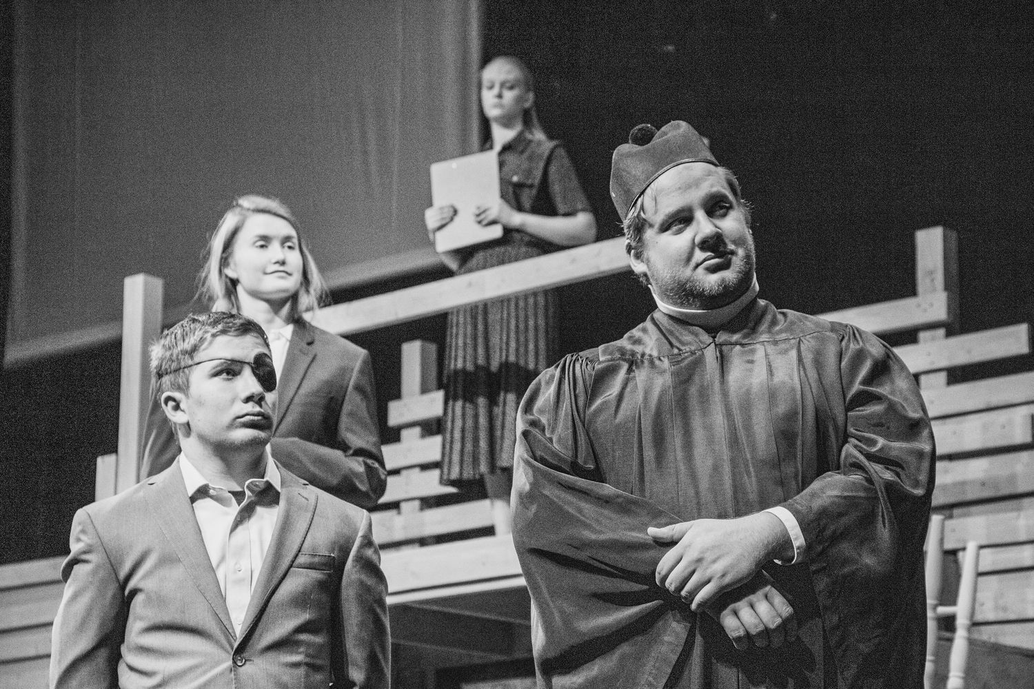 Group of performers in formal attire on stage during theatrical production.