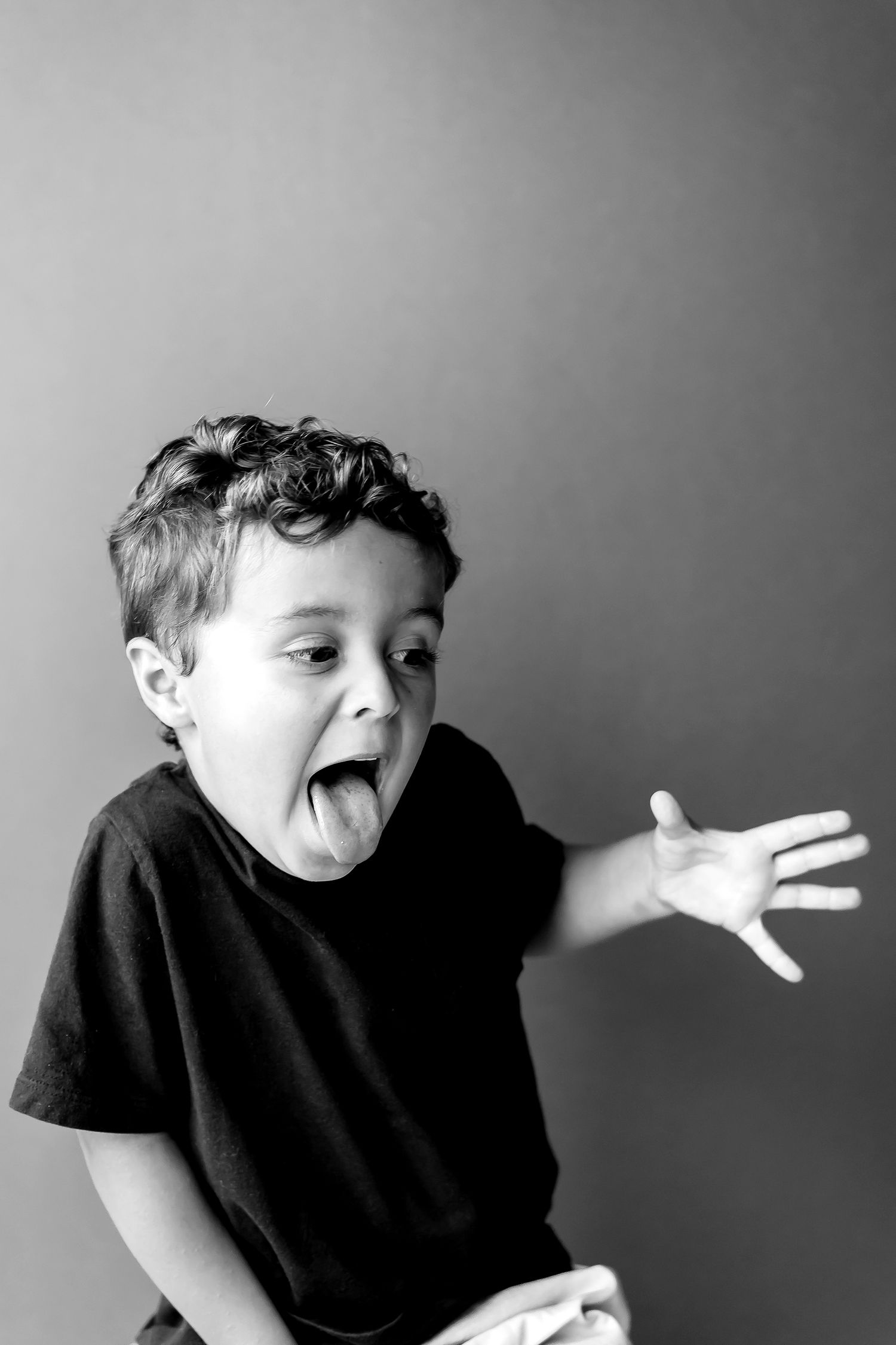 Black and white photo series showing a child in a dark shirt playfully sticking out their tongue and making silly expressions.