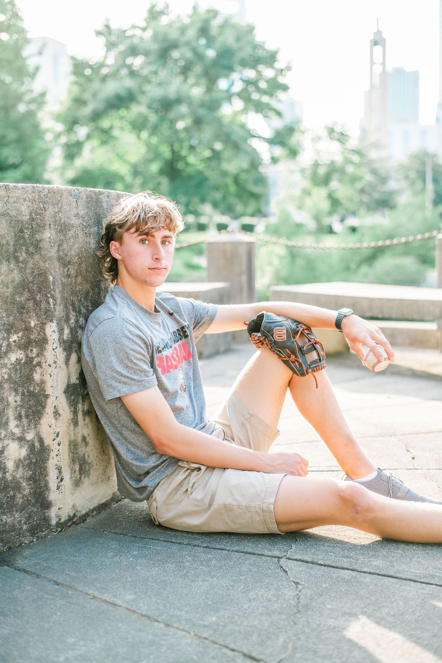 Person relaxing on a concrete ledge in an urban park setting on a sunny day.