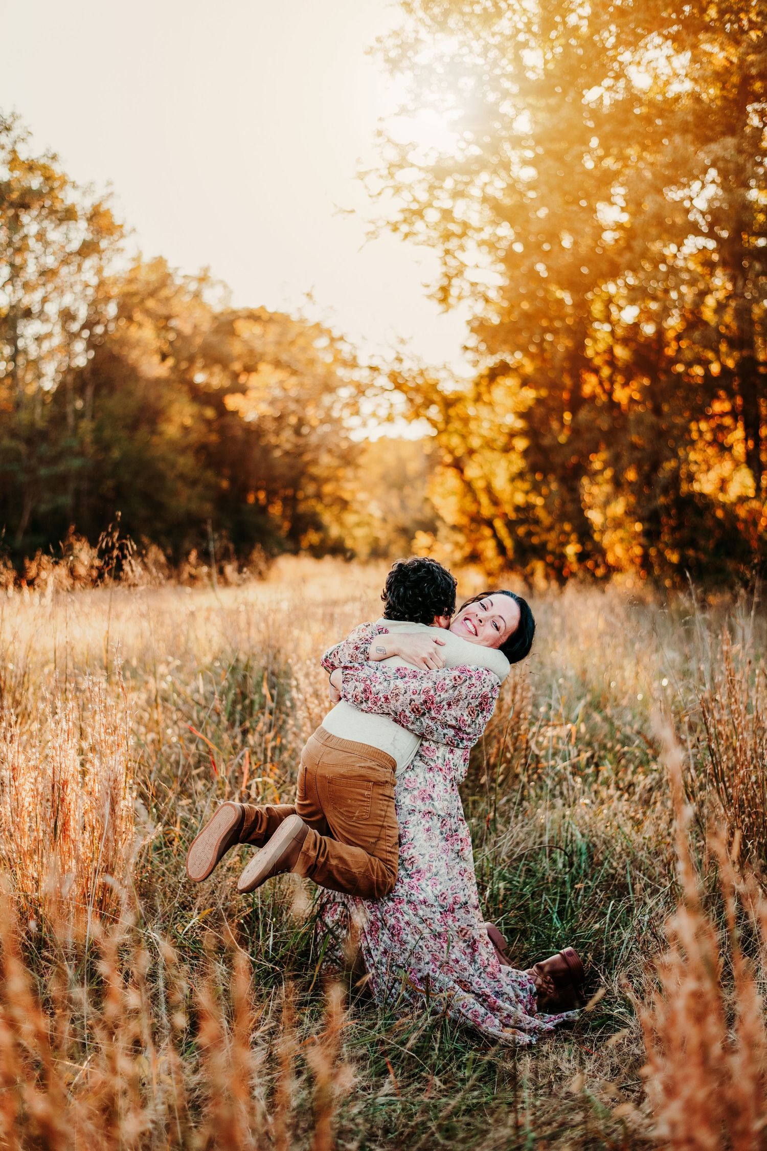A couple embraces joyfully in a sun-drenched meadow during golden hour.