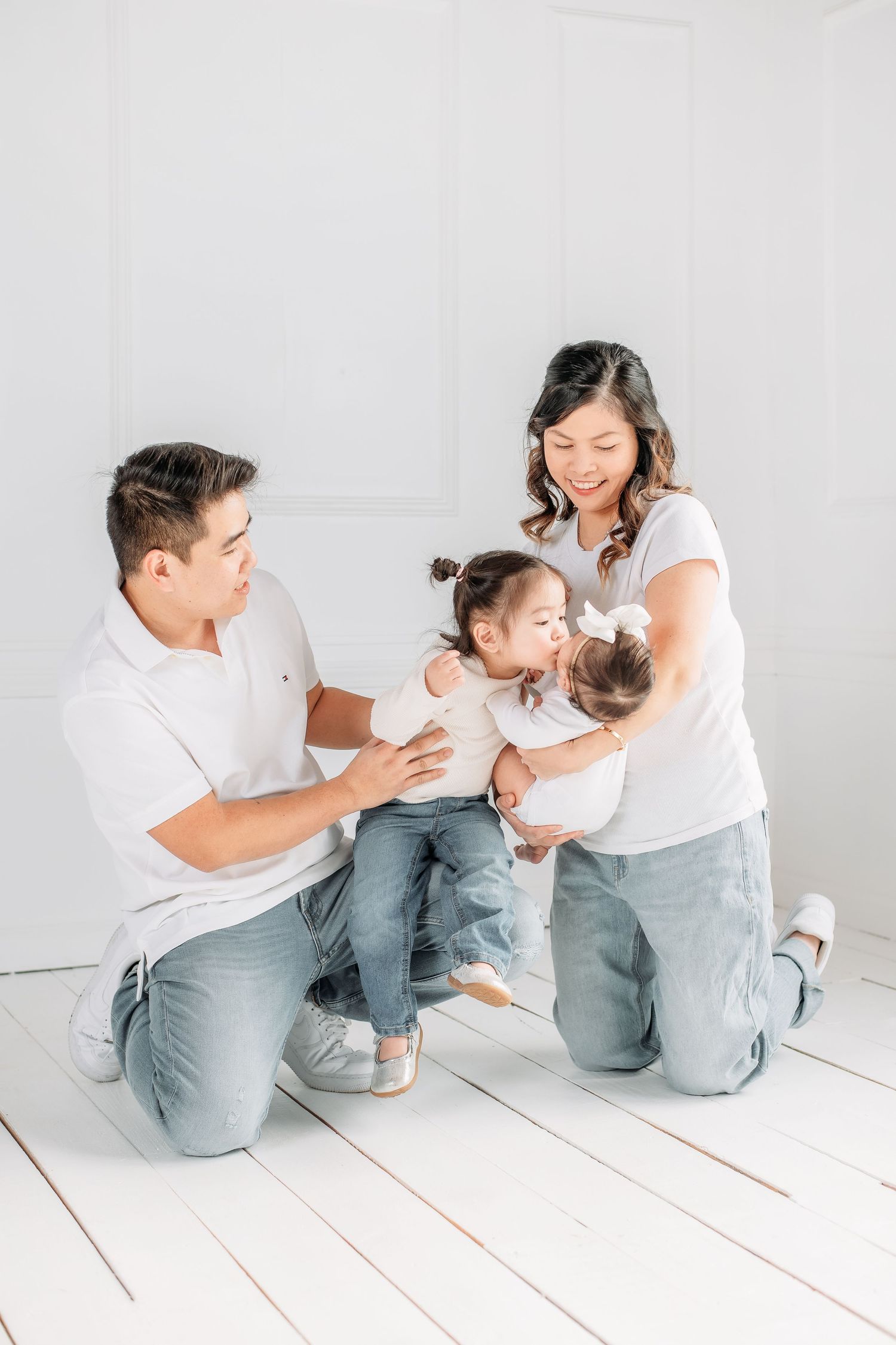 A family in matching white tops and jeans plays together on a white wooden floor.