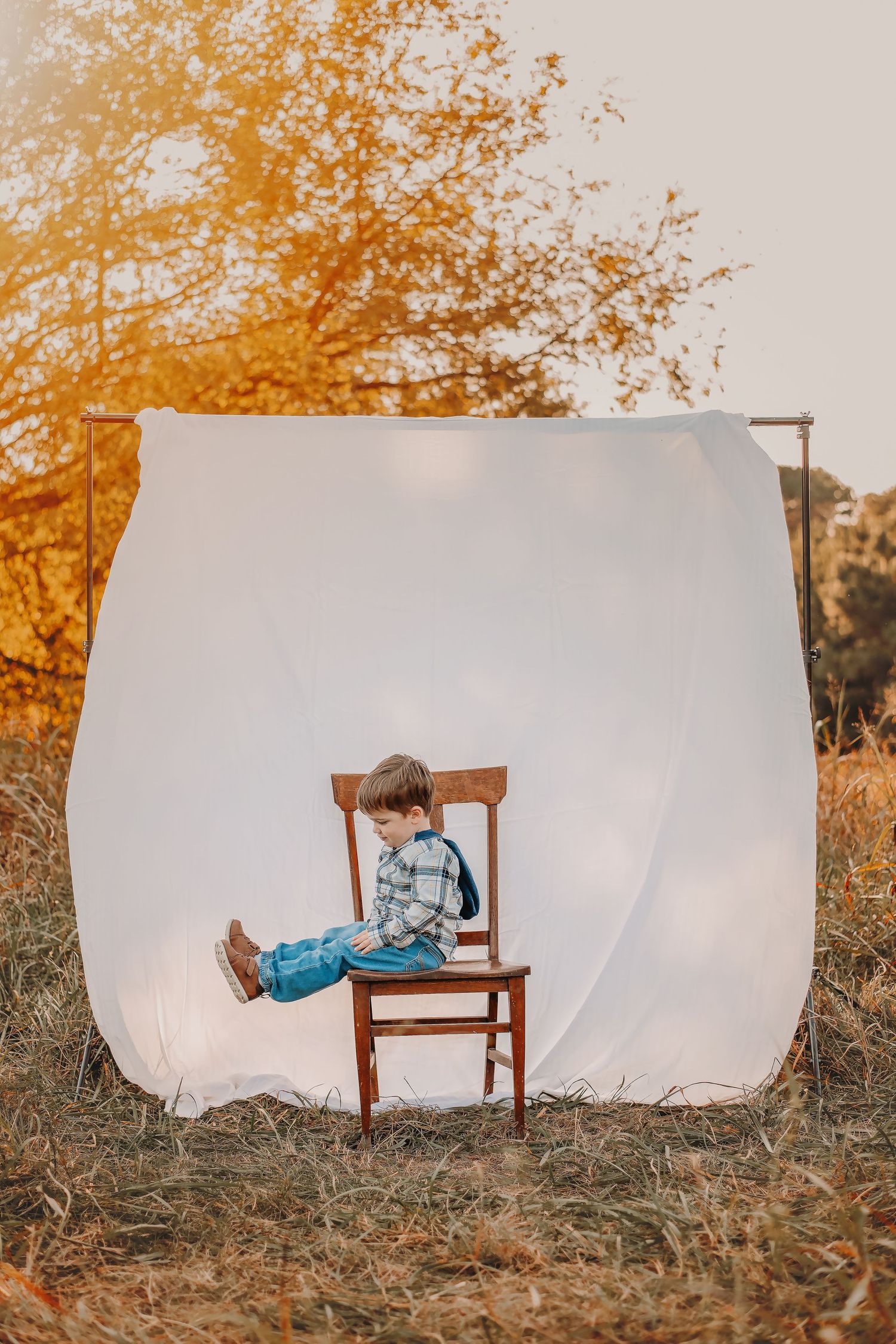 A white backdrop set up outdoors with a wooden chair against autumn foliage in golden afternoon light.