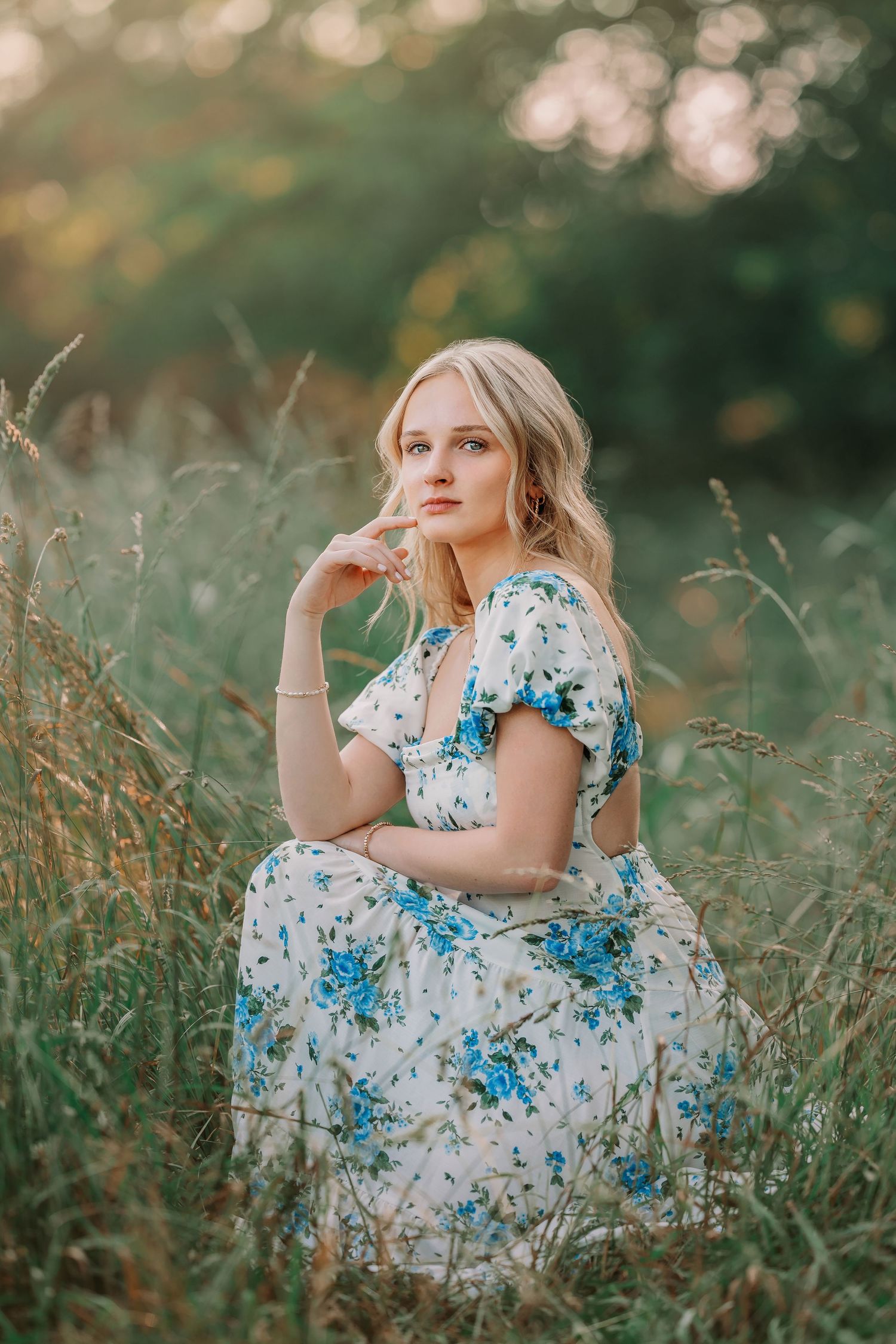 Person in floral dress sitting gracefully in tall summer grass during golden hour.