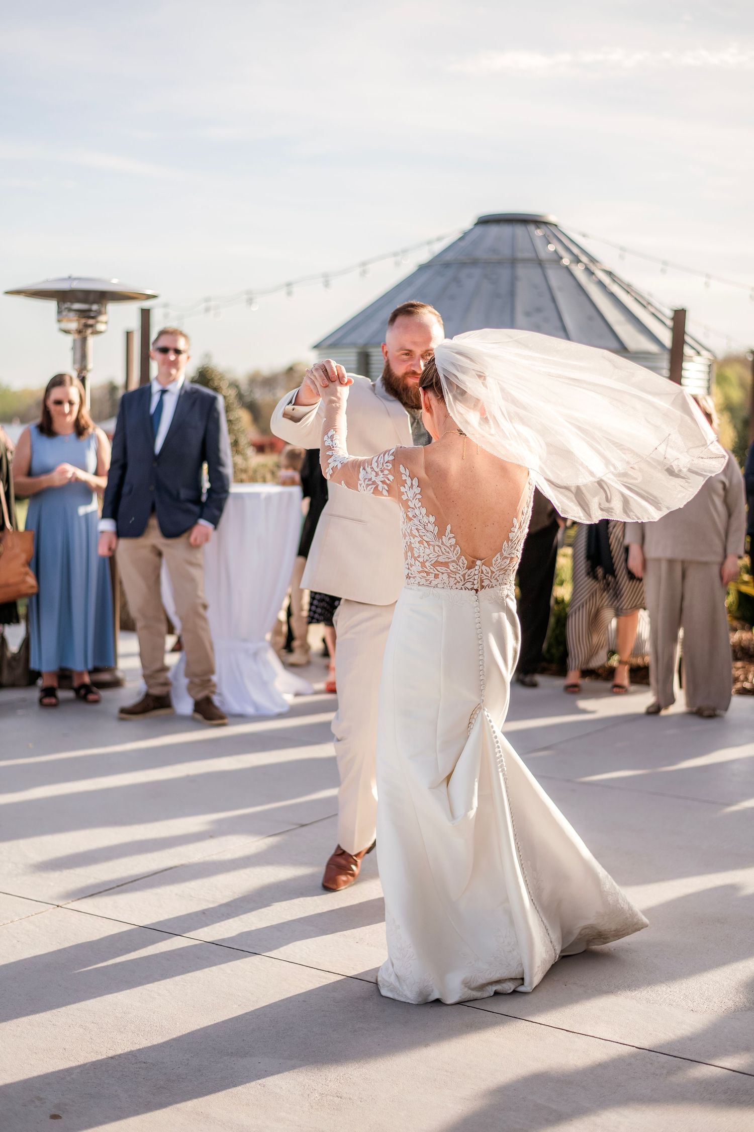 Bride and groom share first dance outdoors at wedding reception with guests watching.