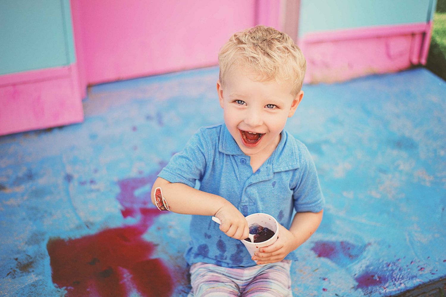 A child in a blue shirt laughs while playing with colorful powder during a fun outdoor activity.