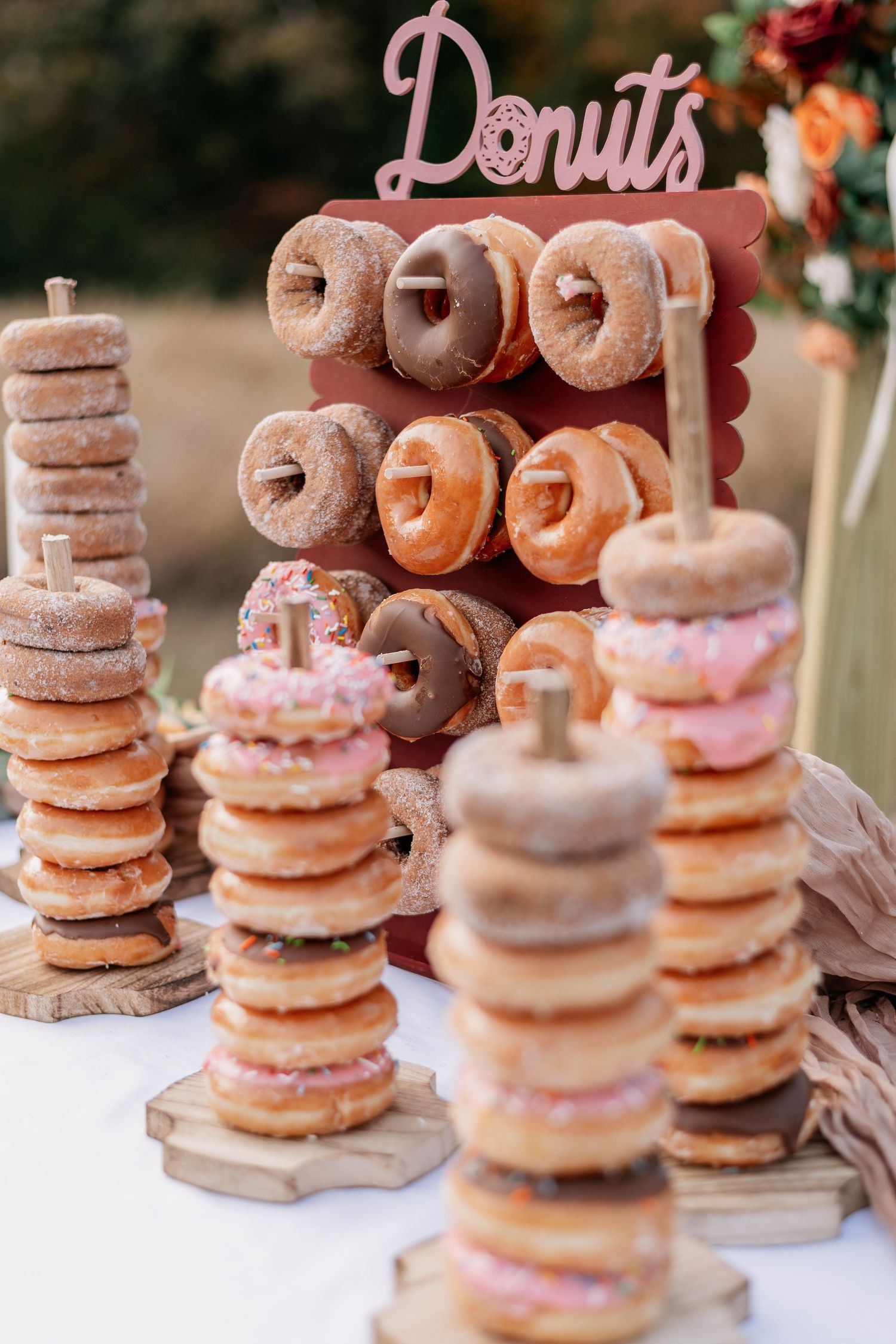 Elegant donut wall display with stacked donuts on wooden stands, featuring glazed, chocolate, and pink frosted varieties.
