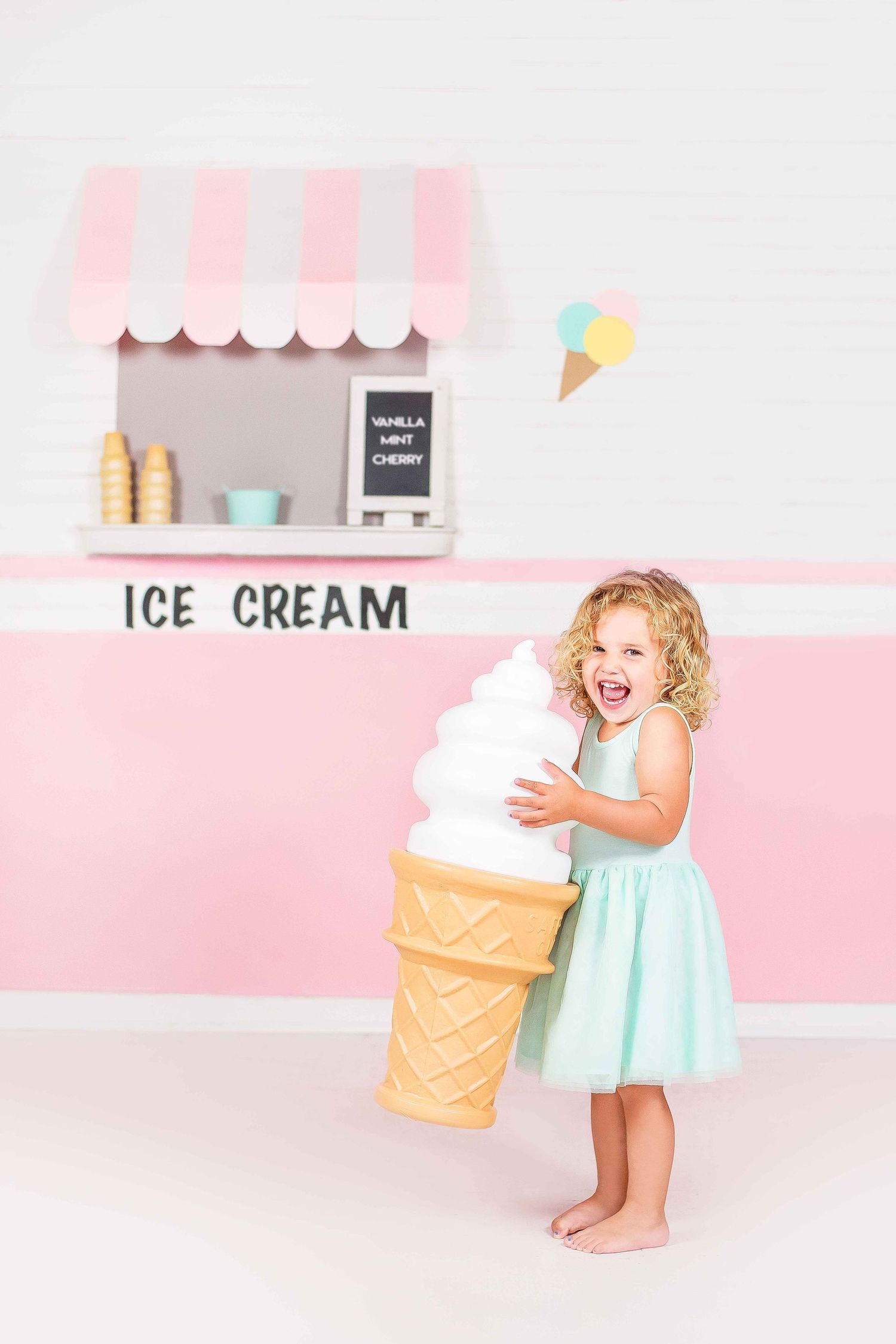 Playful scene in pink and white ice cream shop setting with mint dress and large decorative cone prop.