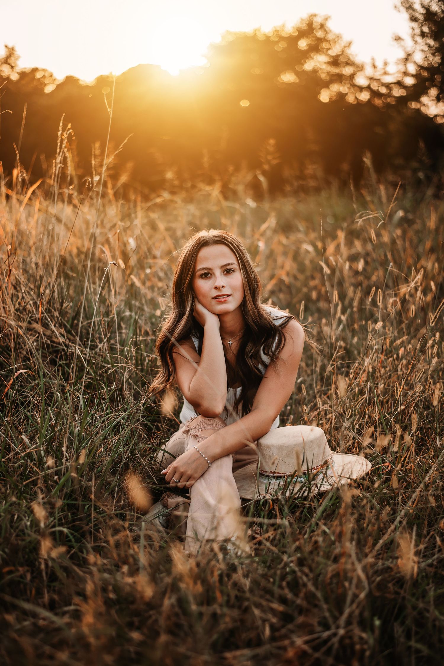 Woman sitting thoughtfully in field during golden hour sunset.