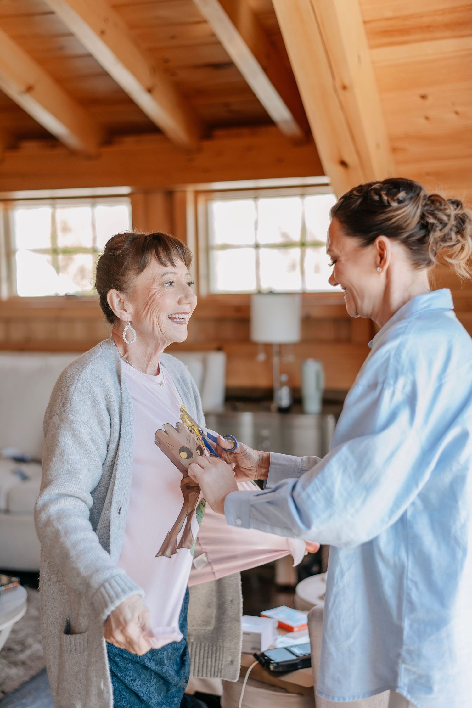 Elderly woman smiling as caregiver assists her indoors in a warm wooden home setting.