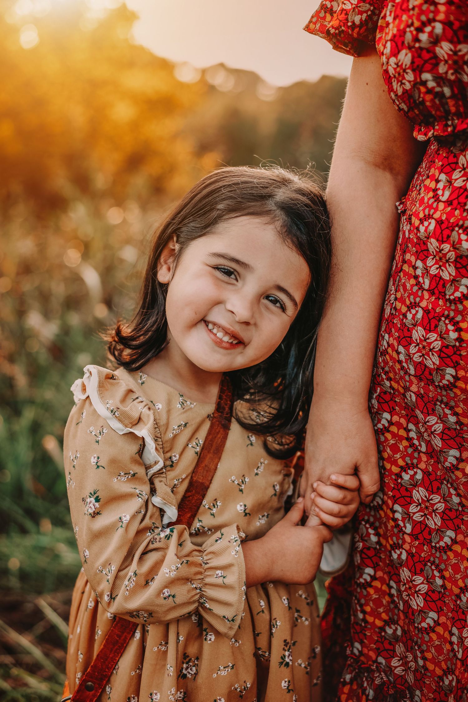 Young girl in floral dress holding parent's hand during golden hour photoshoot in Mooresville NC.