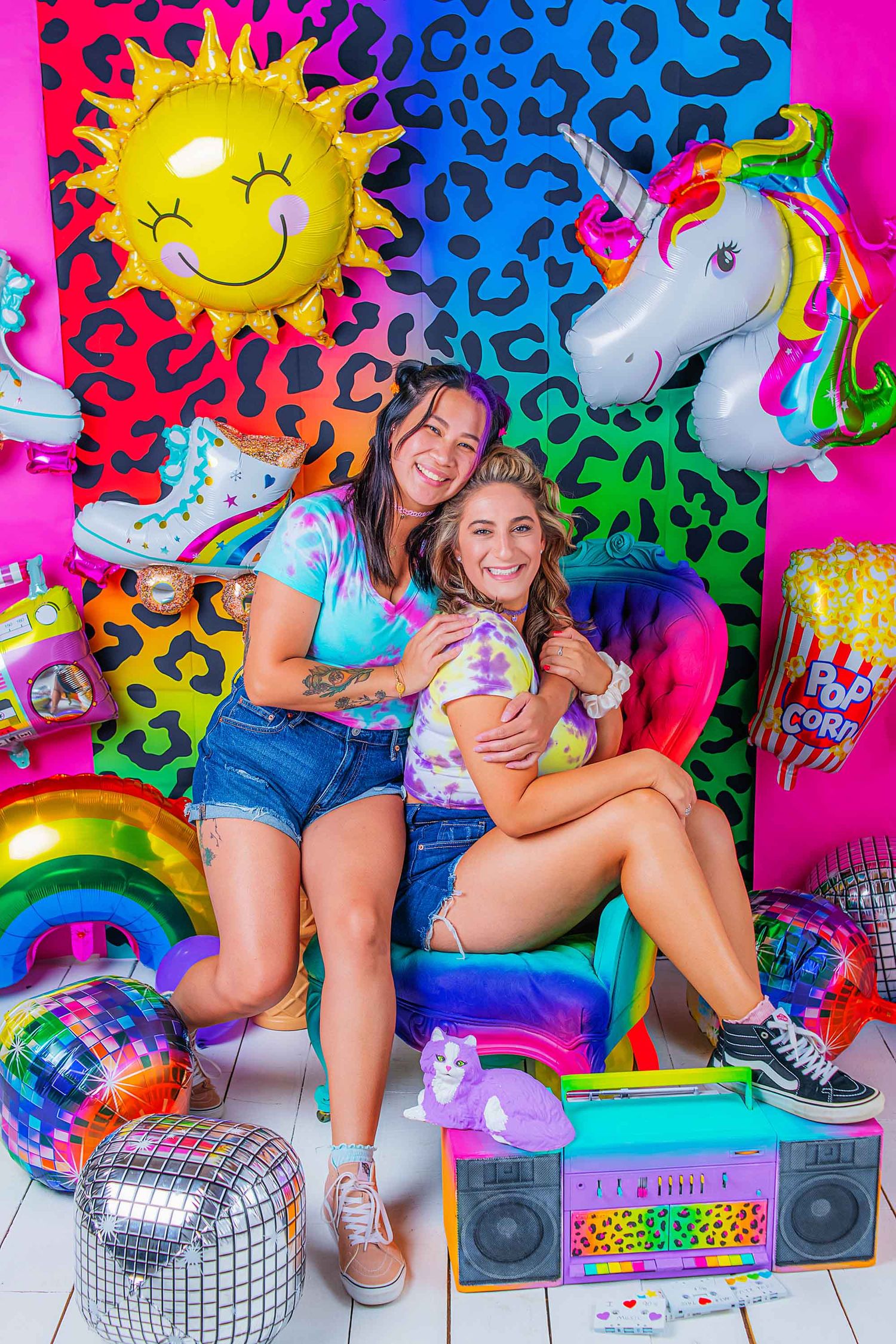 Colorful retro 90s style photo shoot with neon leopard print backdrop, disco ball, and unicorn plush toys.