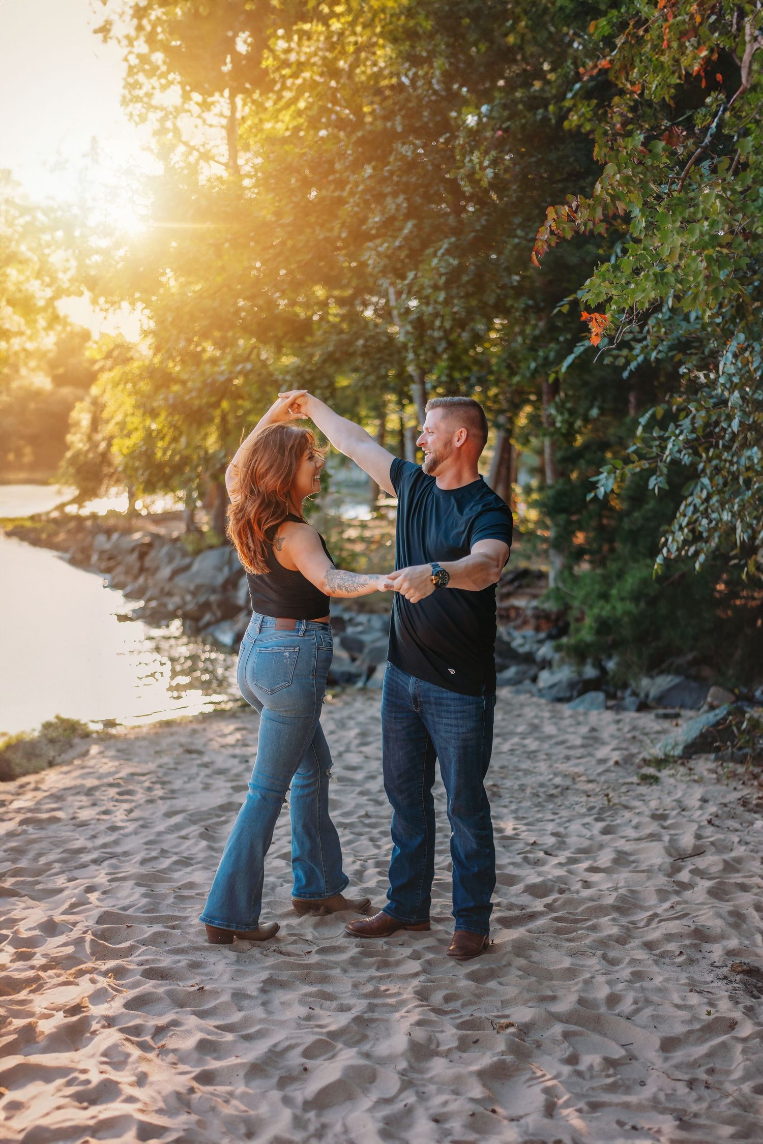 Dancing couple shares romantic moment on beach with golden sunlight filtering through trees.