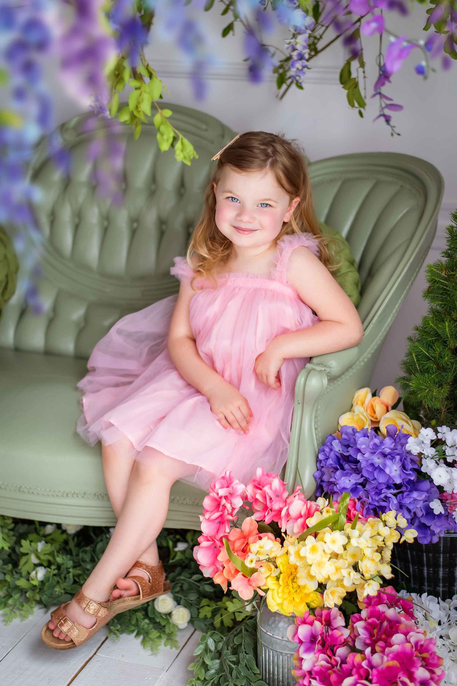 A child in a pink tulle dress poses with vibrant spring flowers including purple, yellow and coral blooms in a garden setting.