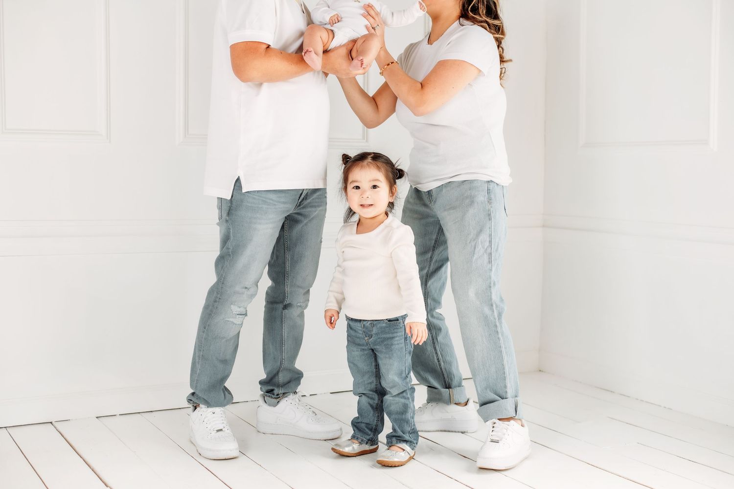Family portrait of matching outfits with white shirts and jeans standing together in a light studio setting.