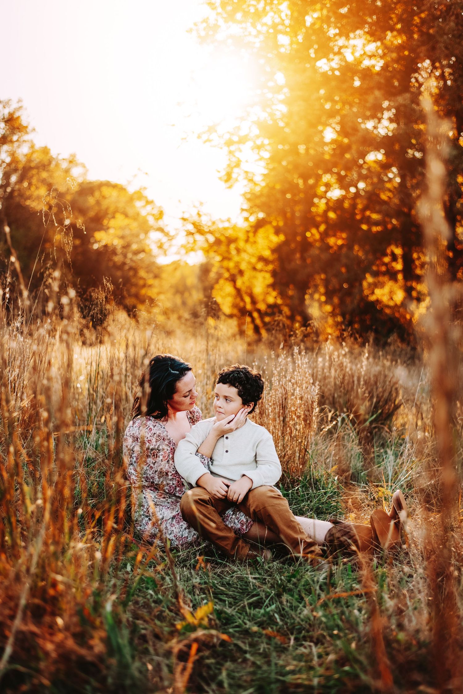A romantic sunset photoshoot in a golden field with tall grass and autumn trees glowing in warm light.