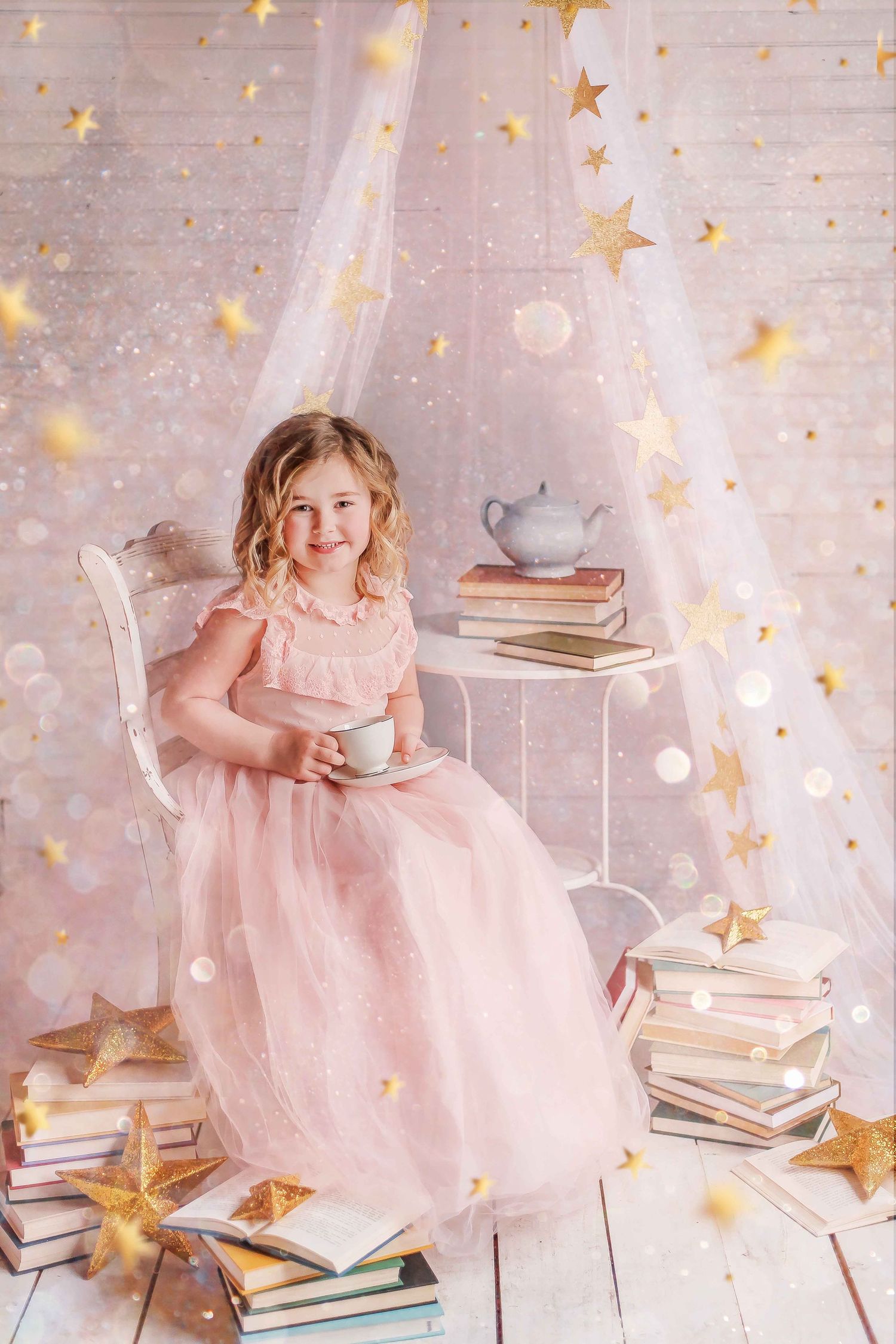 A magical scene with pink dress, stacked vintage books, gold stars and dreamy lighting against a white brick wall.