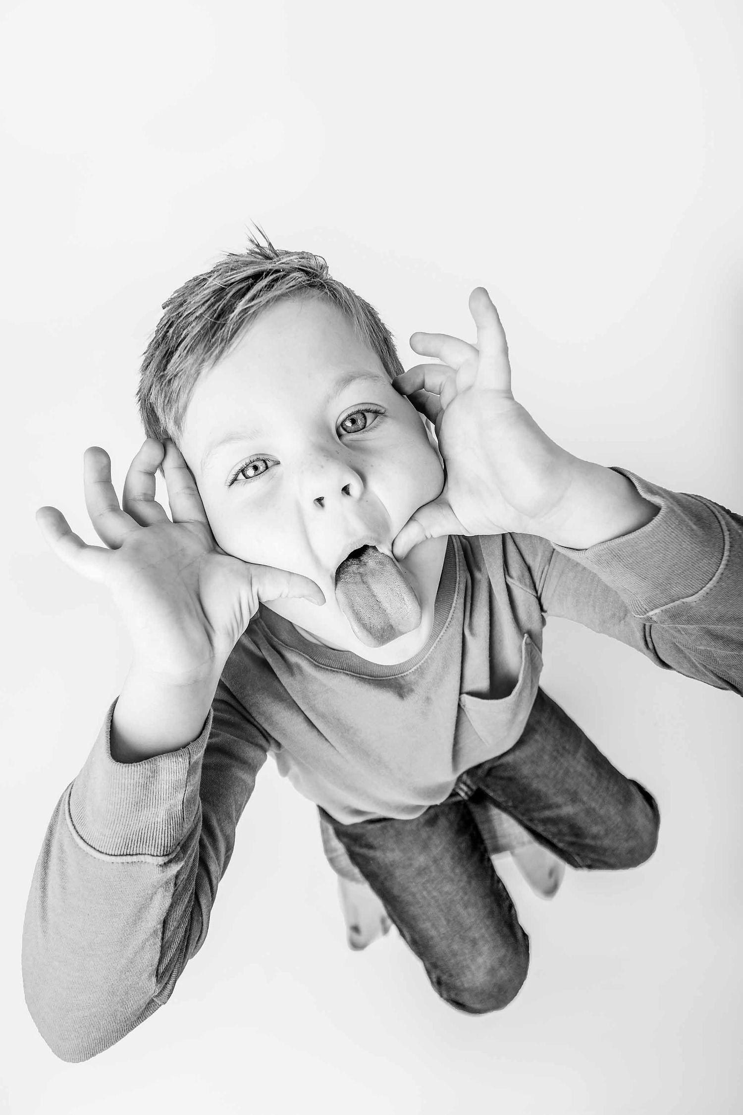 A black and white photo series showing a baby making playful expressions while lying down against a white background.