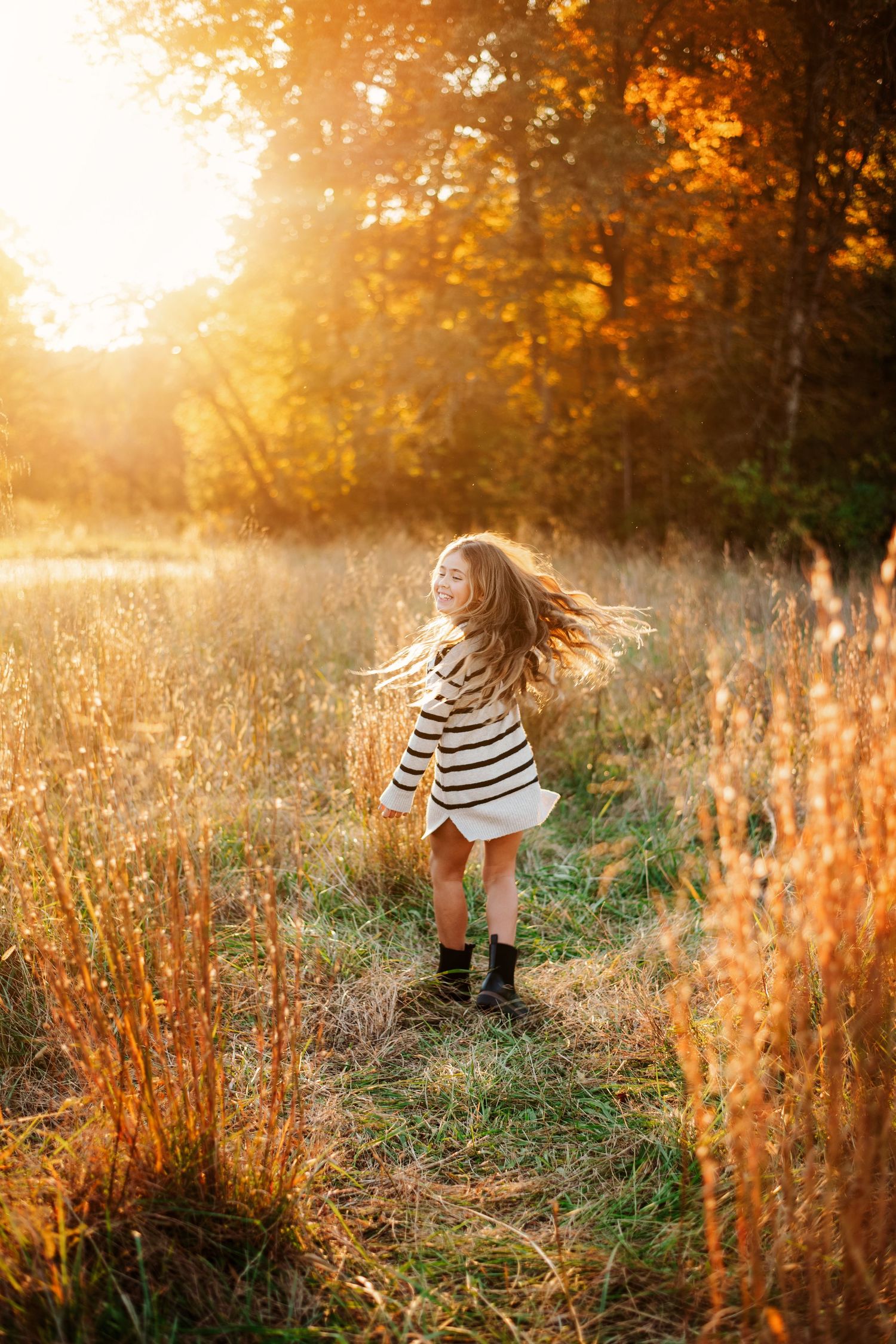 Dancing figure in striped dress twirling through tall grass at sunset.