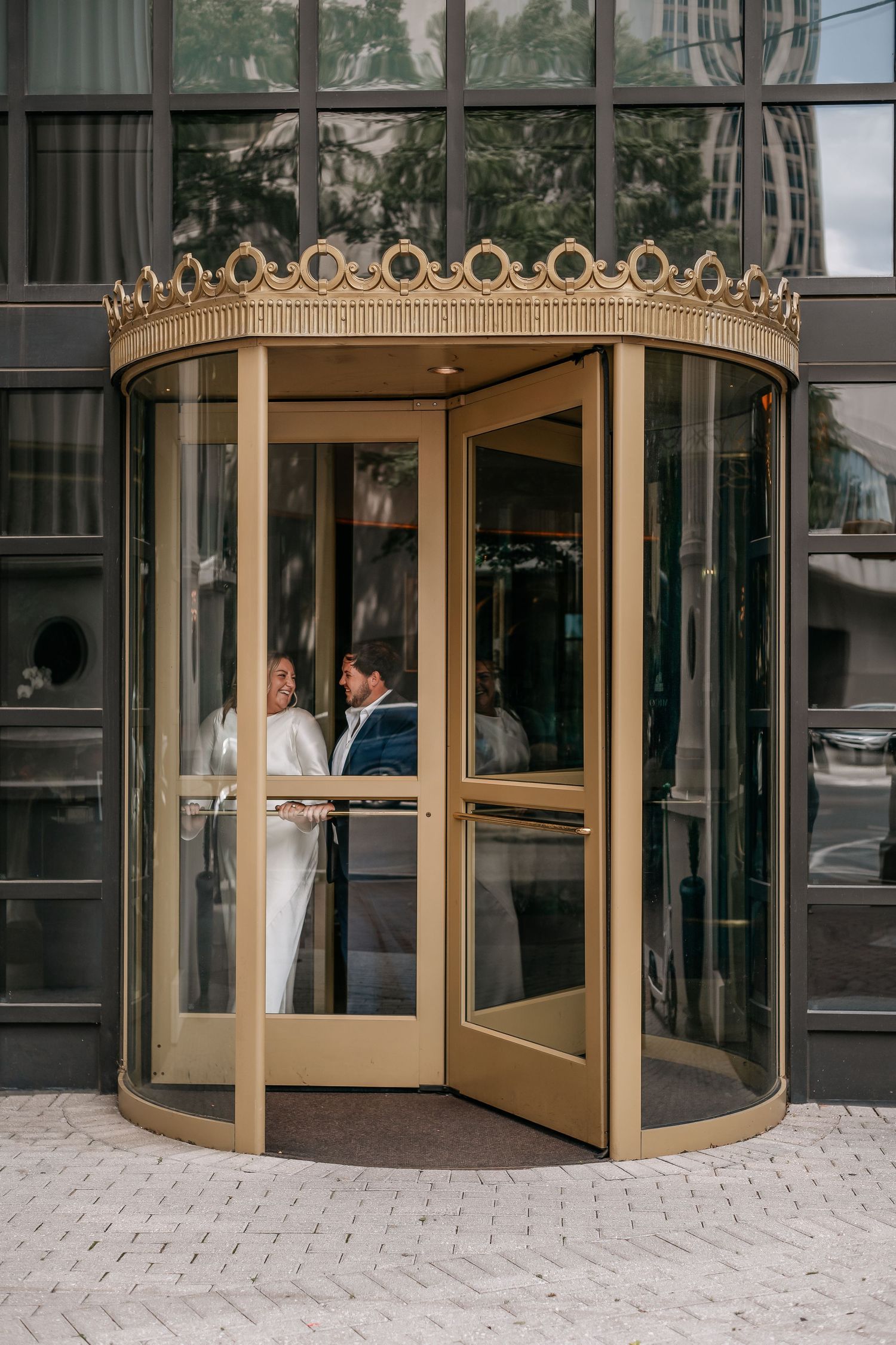 Couple entering a luxury hotel through an ornate gold revolving door with crown-shaped topper.