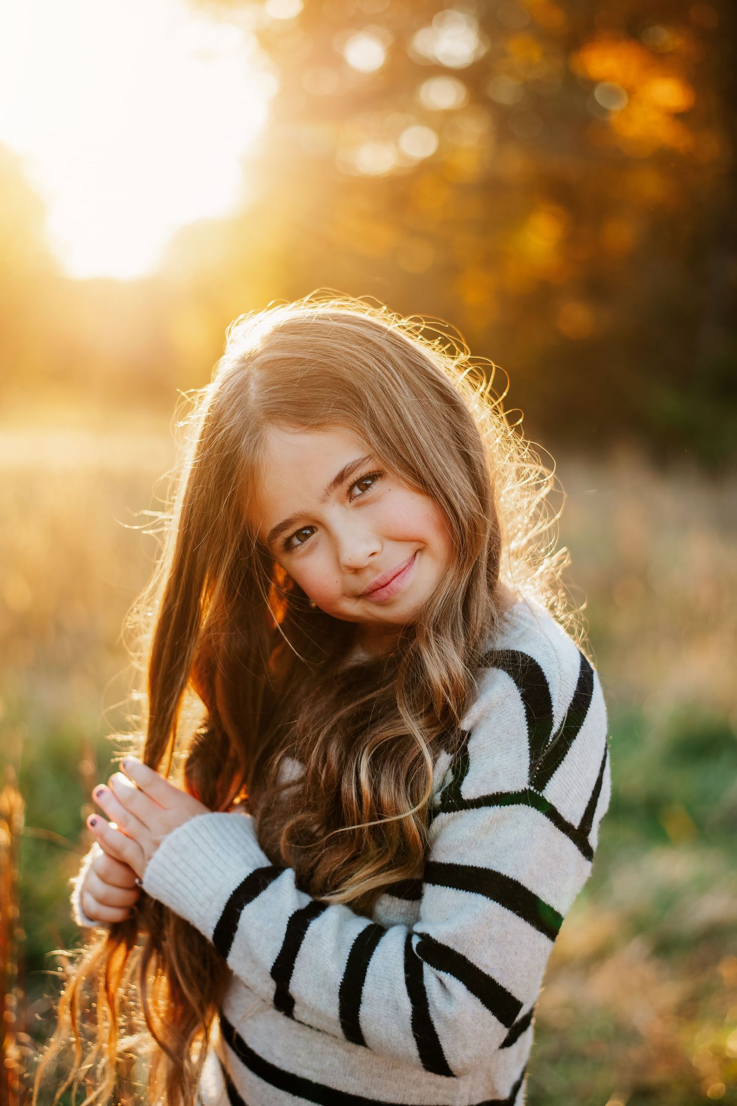 Portrait of a young person in a striped sweater backlit by golden sunset light in an autumn field.