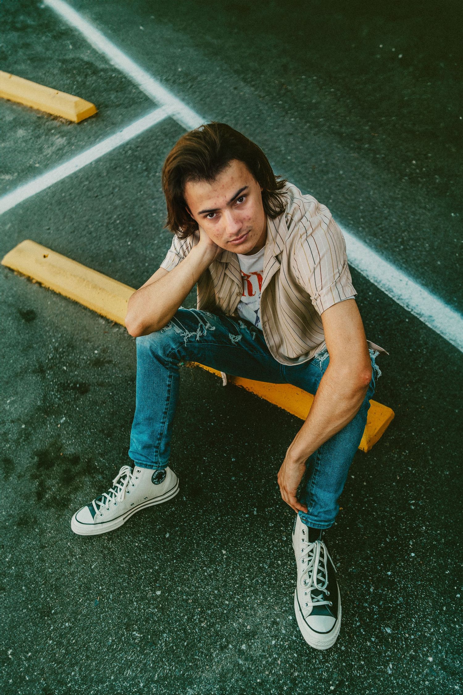 Person in denim and Converse sneakers sitting on yellow parking block in urban setting.