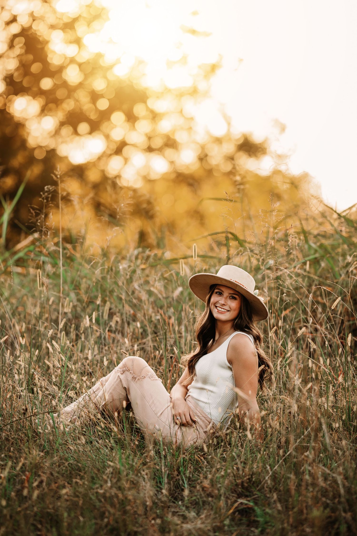 Woman wearing hat relaxing in golden sunlit field.
