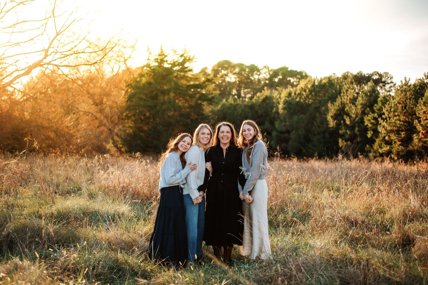 Group poses together in sunlit field during golden hour photoshoot.