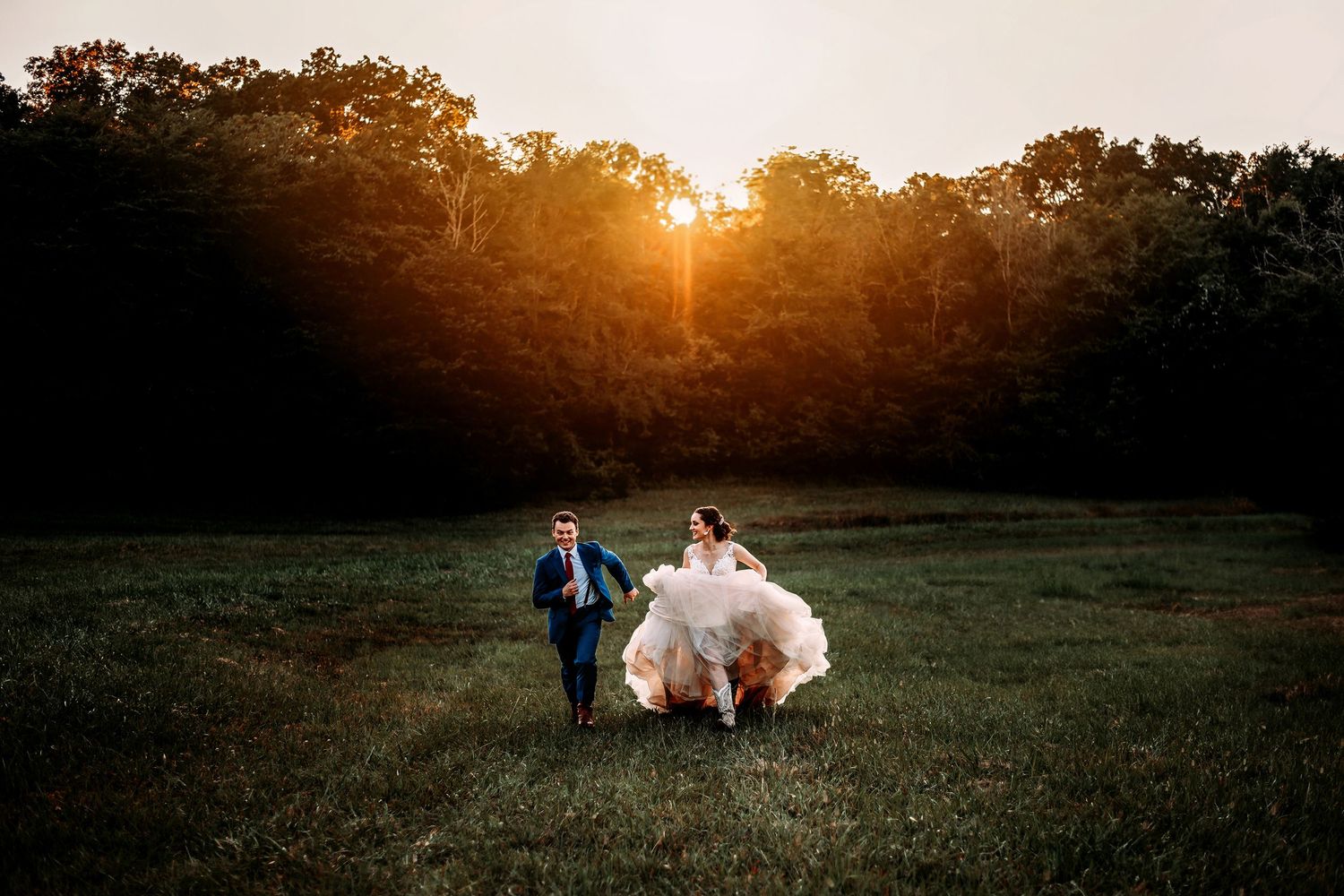 A couple walks through a golden sunset field during a romantic outdoor photo session in the countryside.