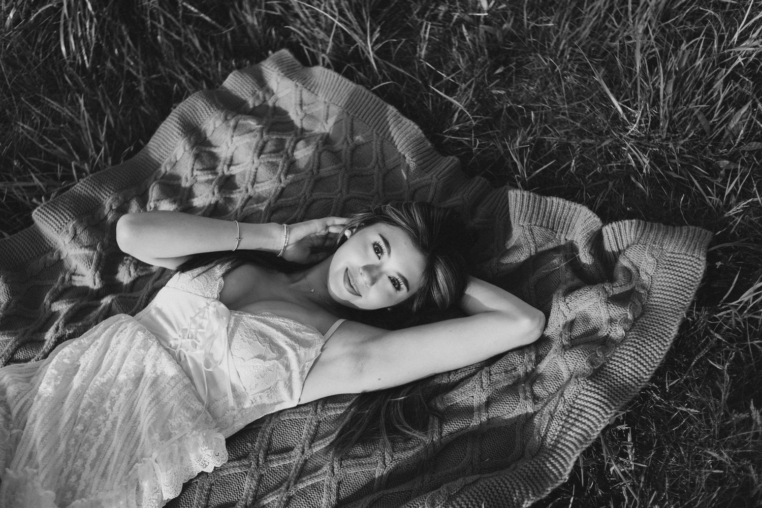 Black and white image of someone reclining on a patterned blanket outdoors.