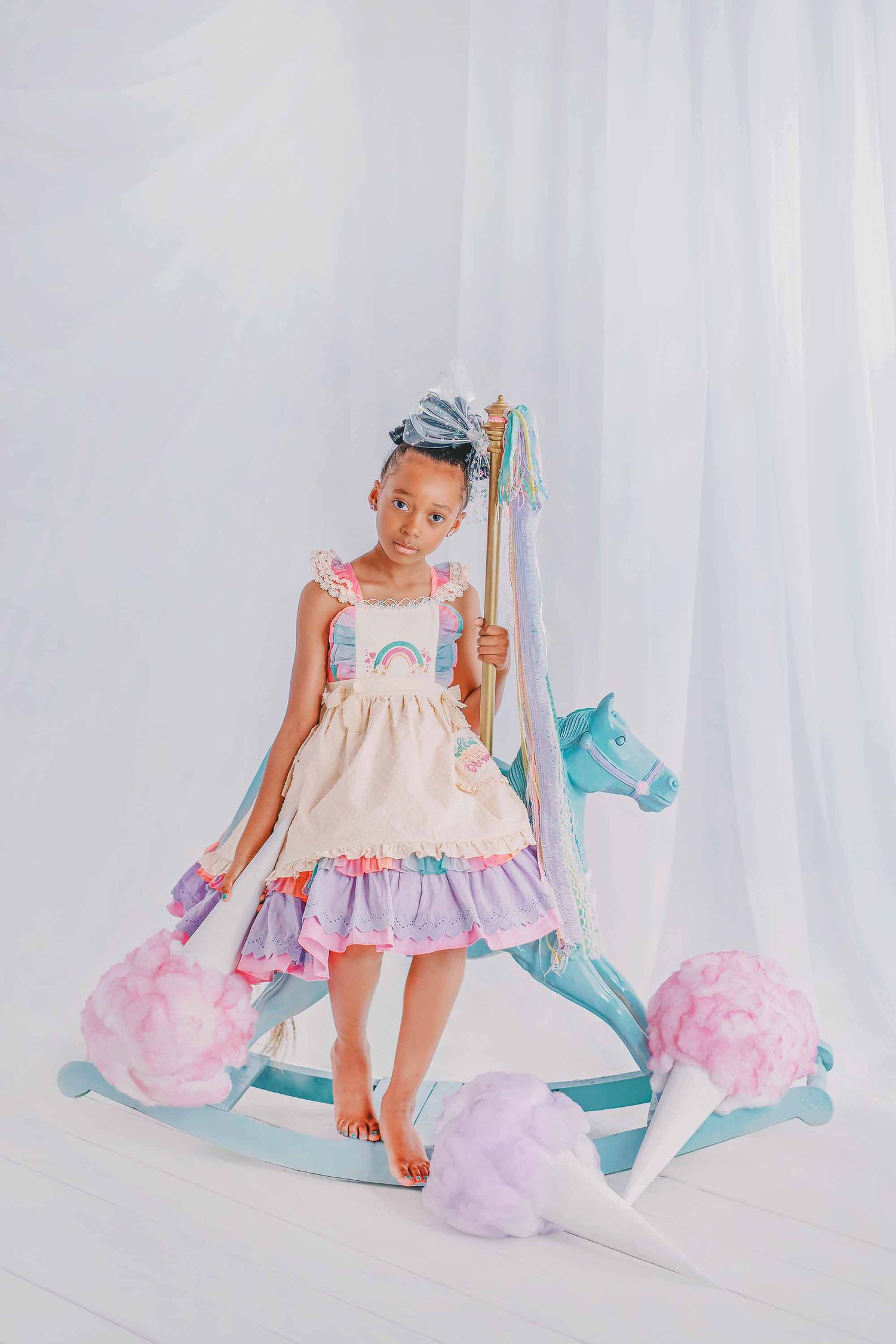Dreamy studio photos of a child in pink dress posing with pastel unicorn decorations against white backdrop.