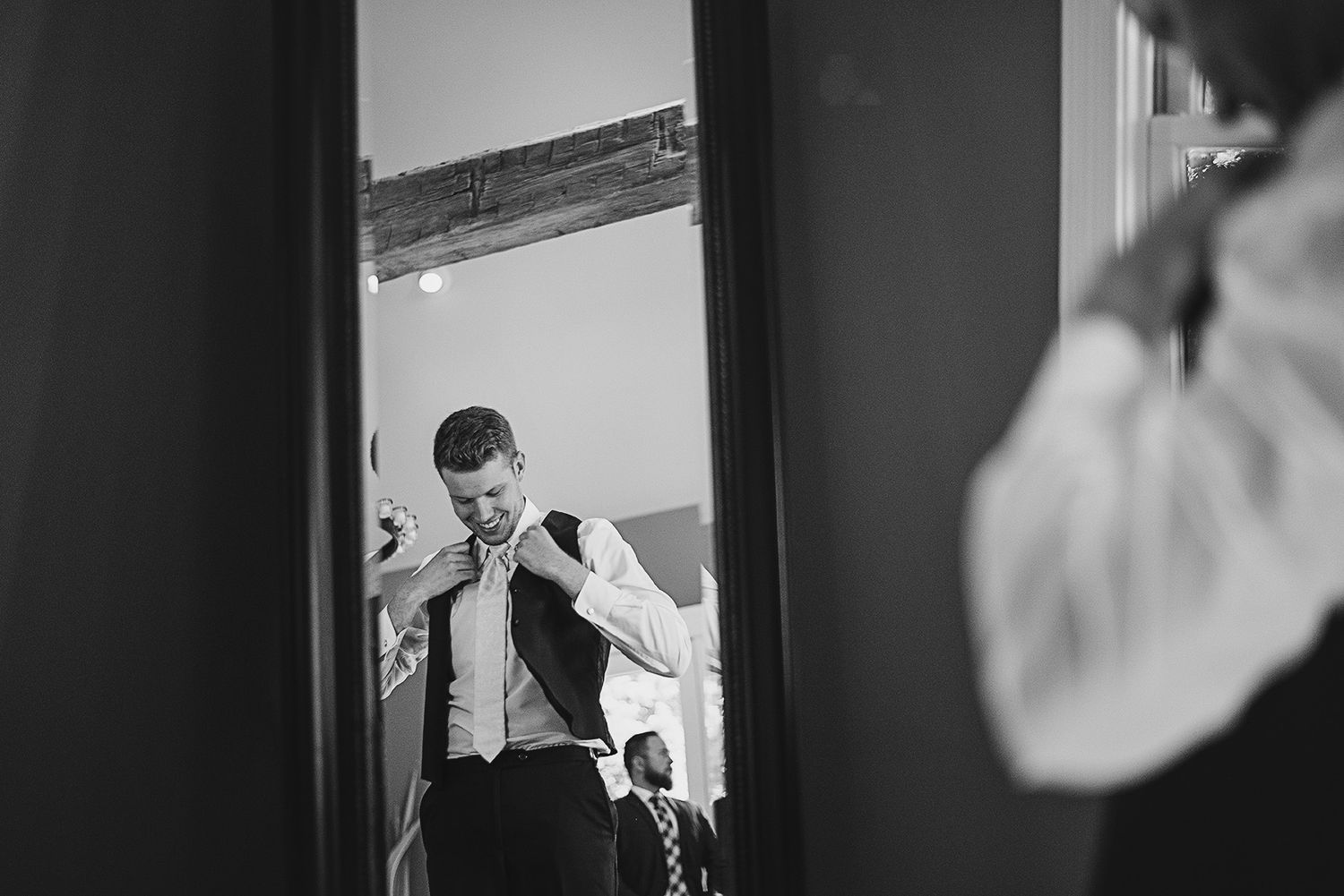 Groom adjusting his vest and tie while getting ready, reflected in a mirror before the wedding ceremony.