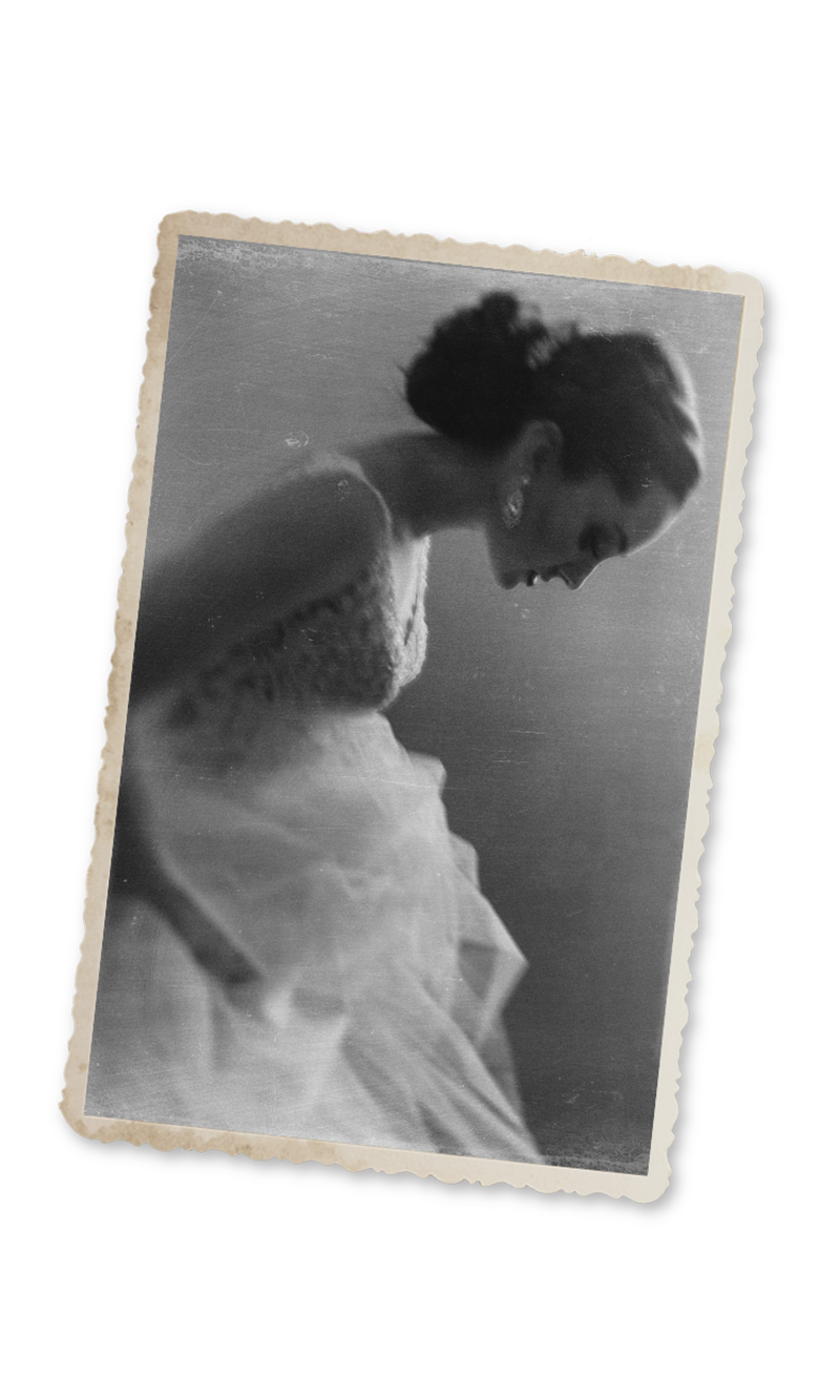 Vintage black and white photo of a bride in a white gown and veil, bowing her head gracefully.