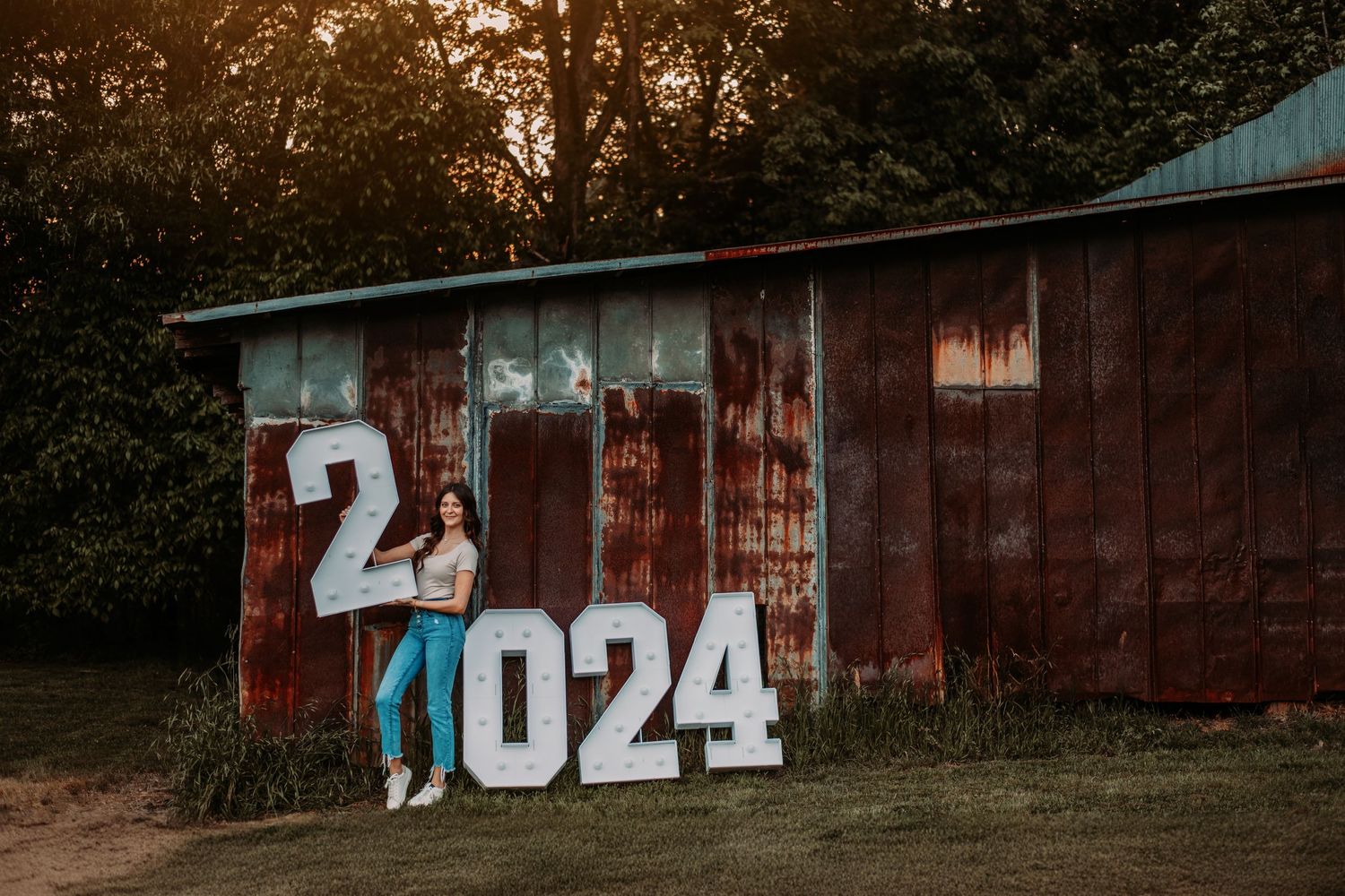 Figure posing with '2024' numbers against rustic red barn wall.