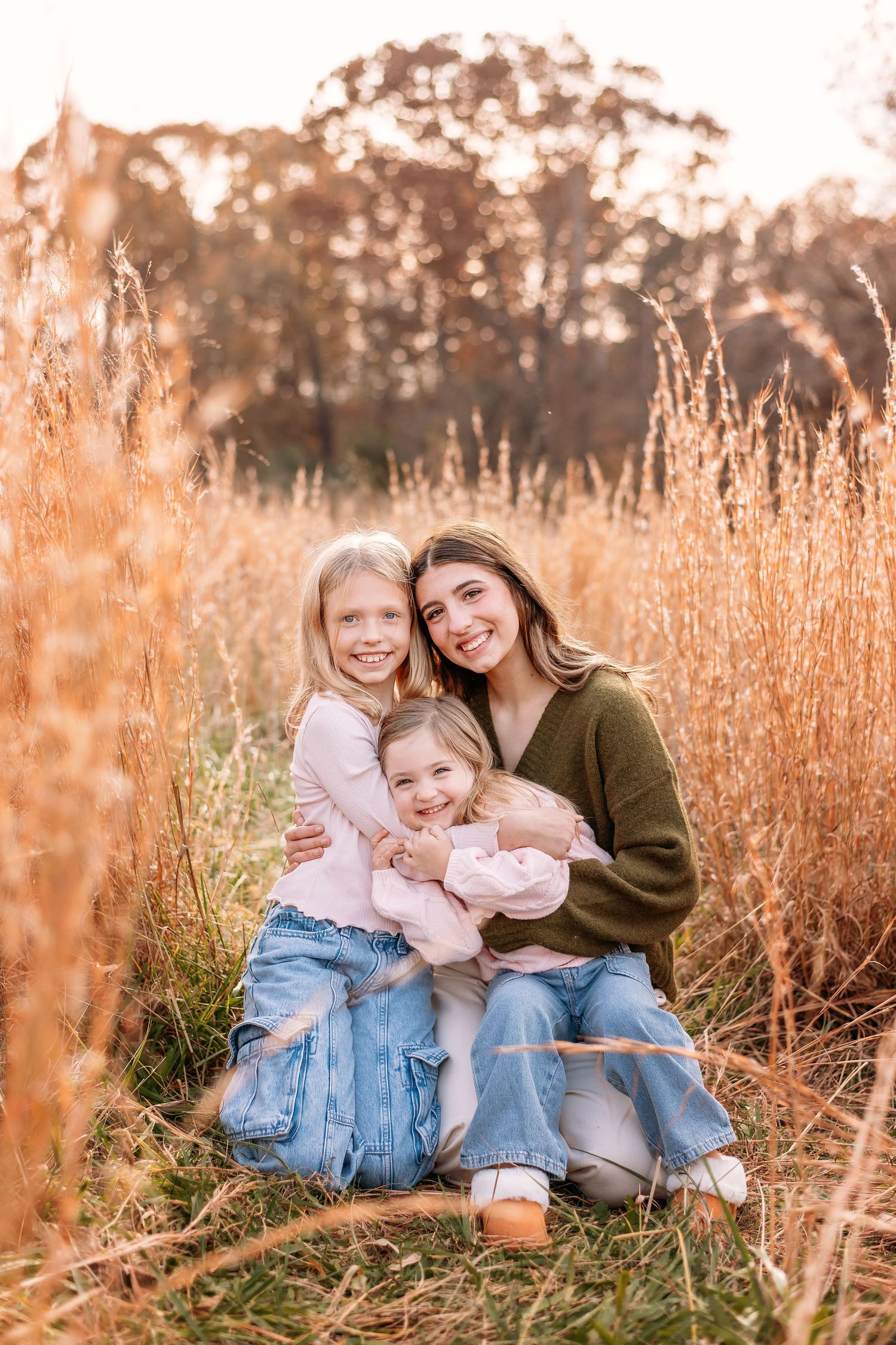 Three people sitting together in a golden field of tall grass during sunset with warm autumn lighting.