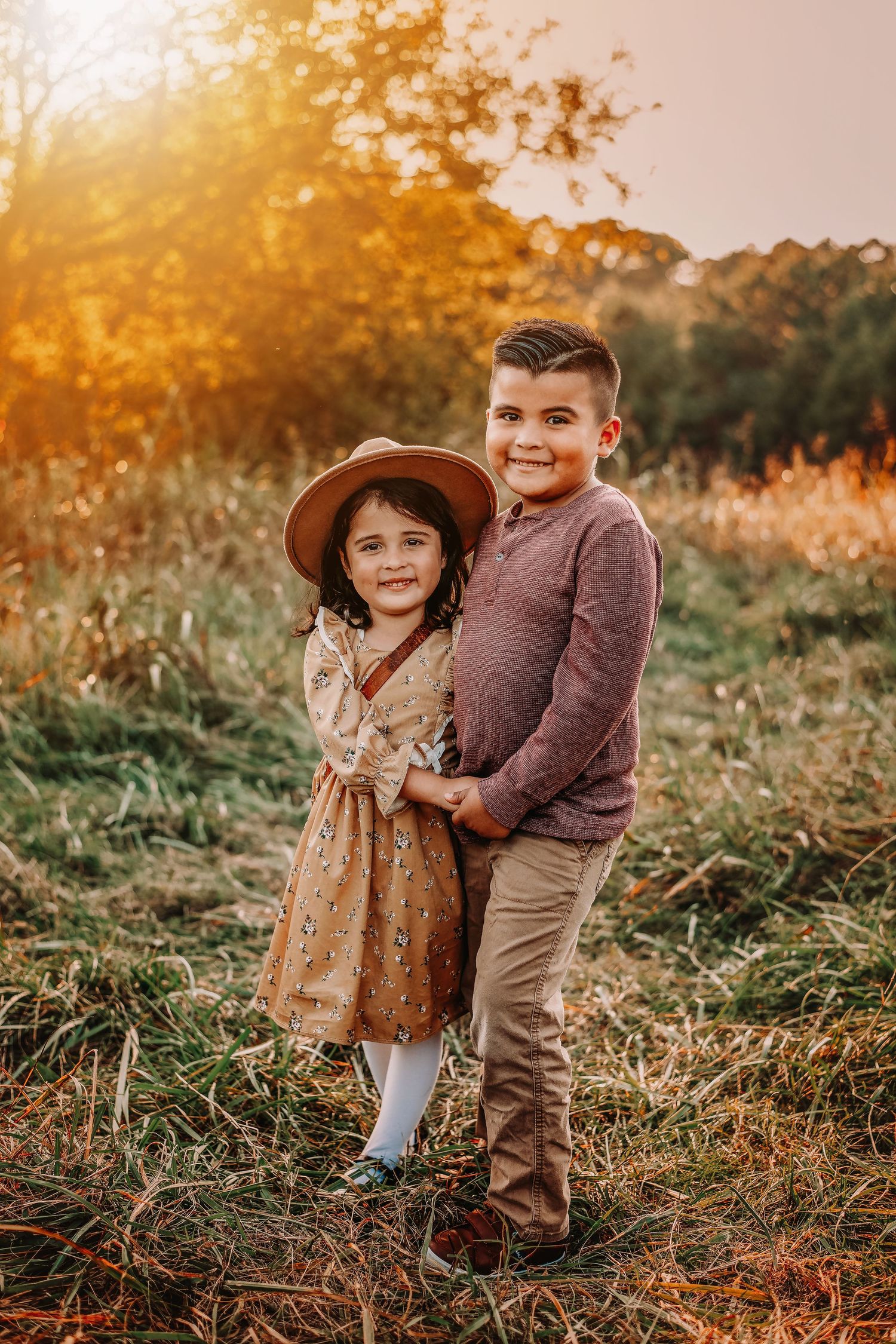 Siblings posing together in autumn field during golden sunset.