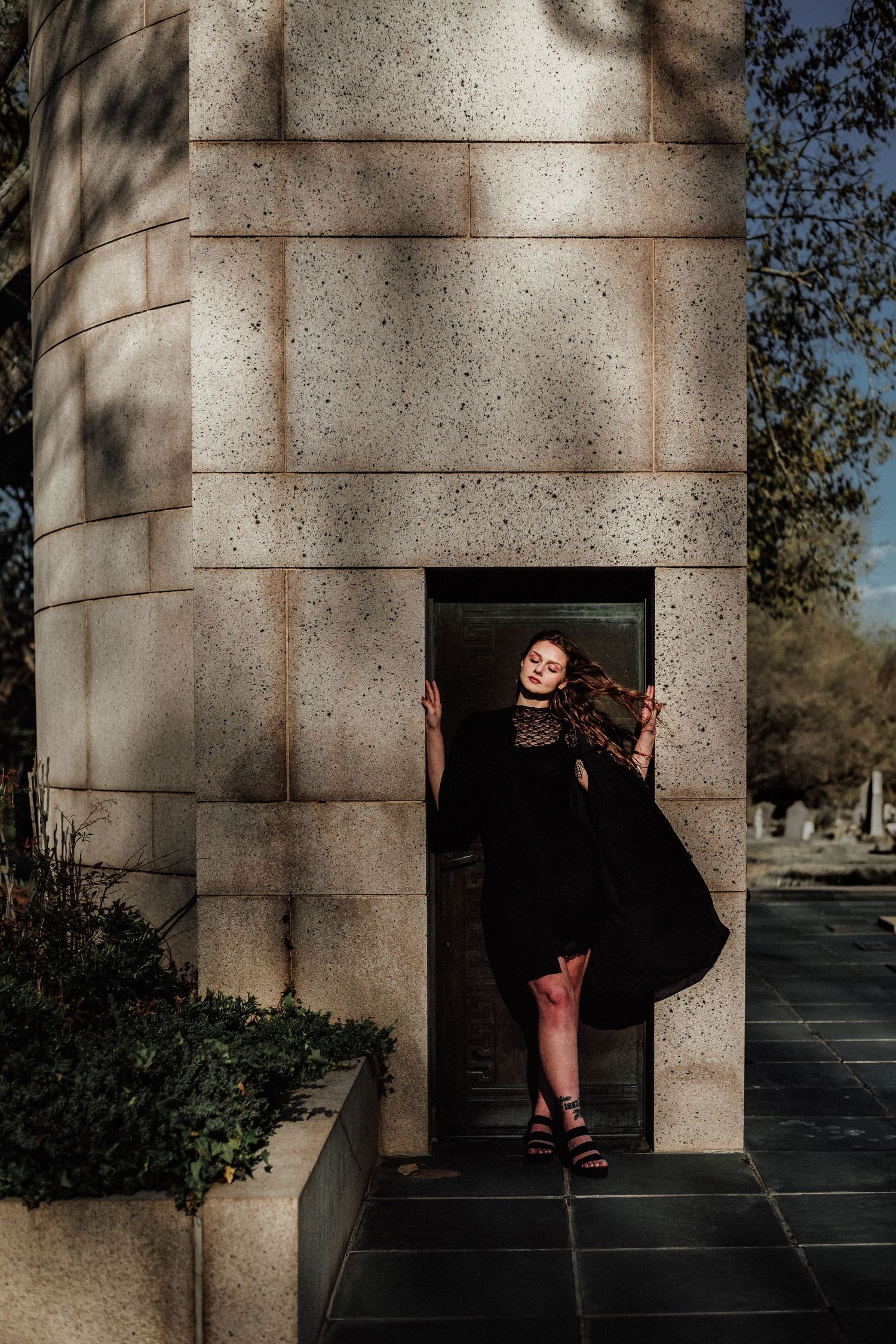 Person in black dress posing dramatically in stone architectural alcove.