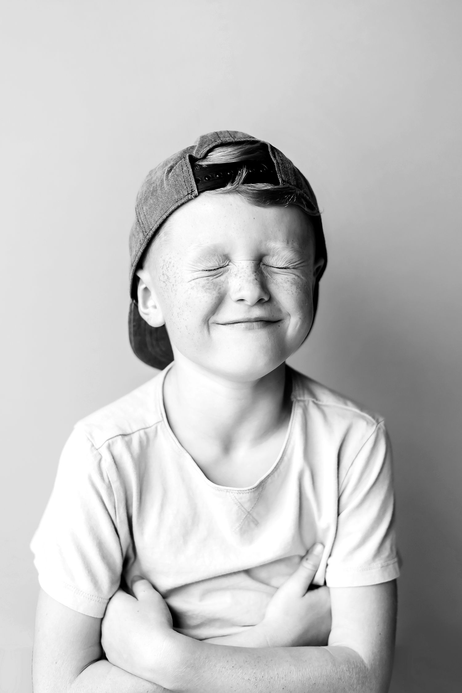 Black and white portrait of smiling child wearing backwards baseball cap.