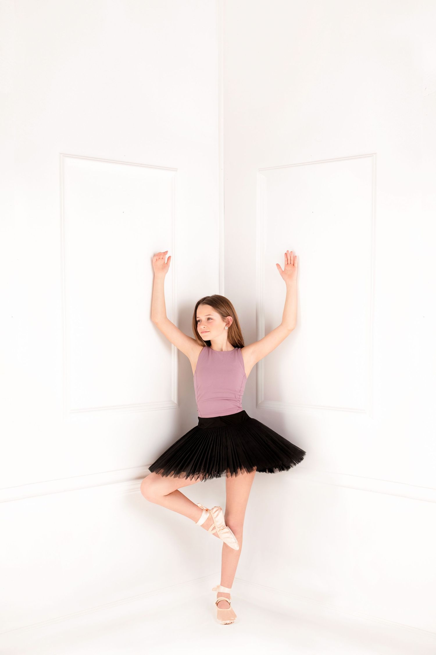 Ballet dancer in pink top and black tutu performs graceful pose against white background.