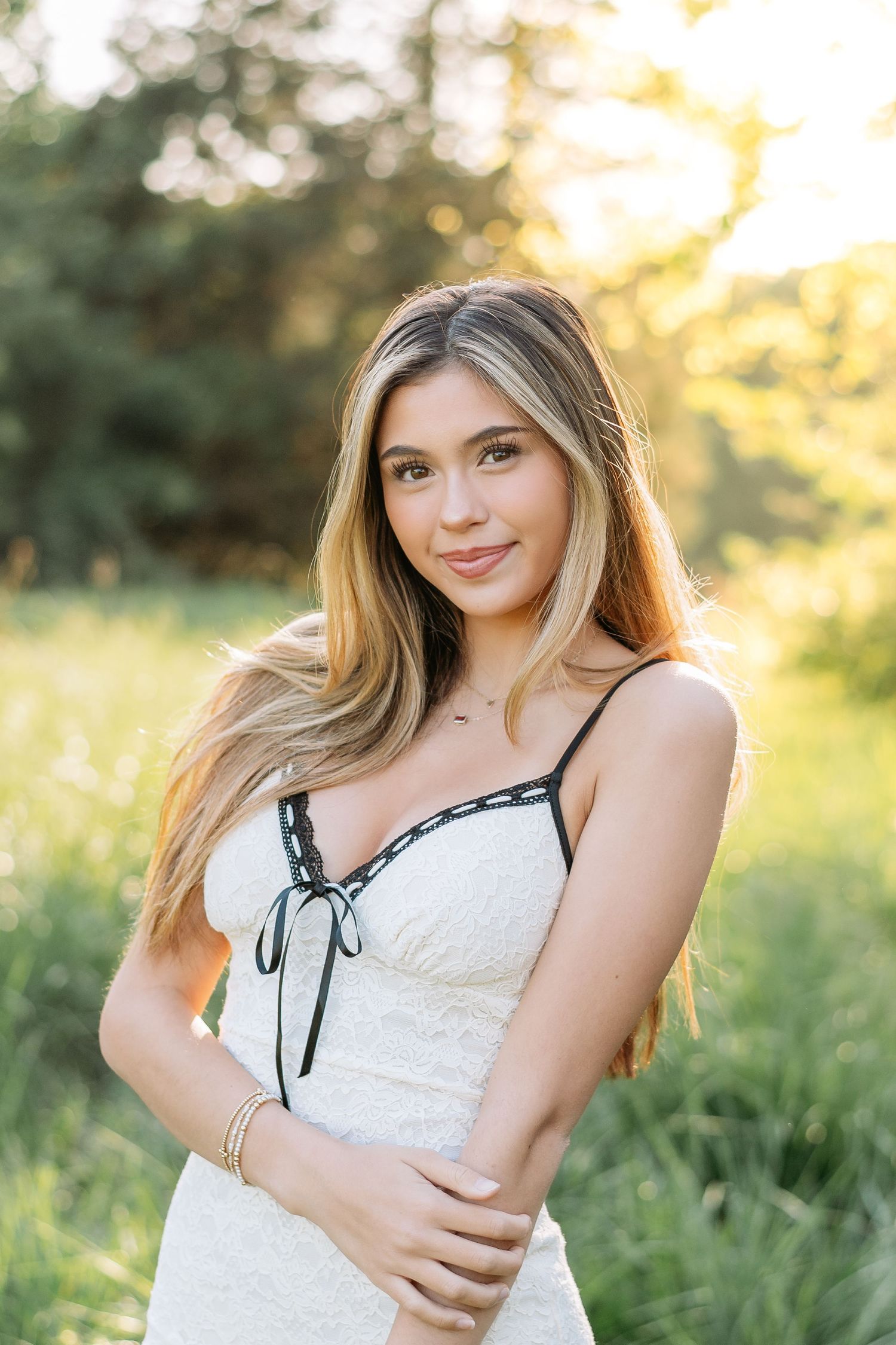 Portrait of woman in white lace dress standing in sunlit meadow at golden hour.