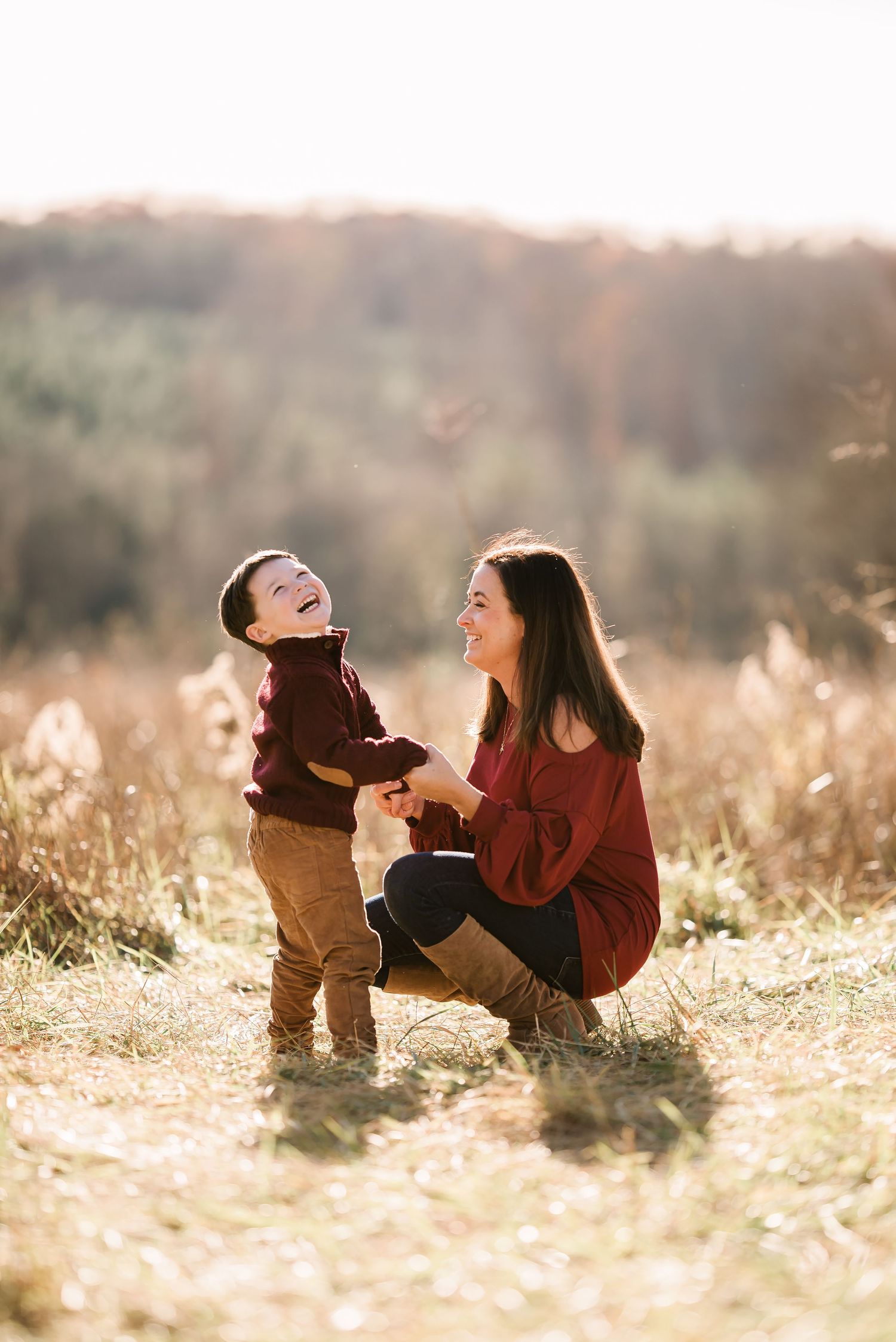 Candid moment of laughter and joy between parent and child in autumn field at sunset.