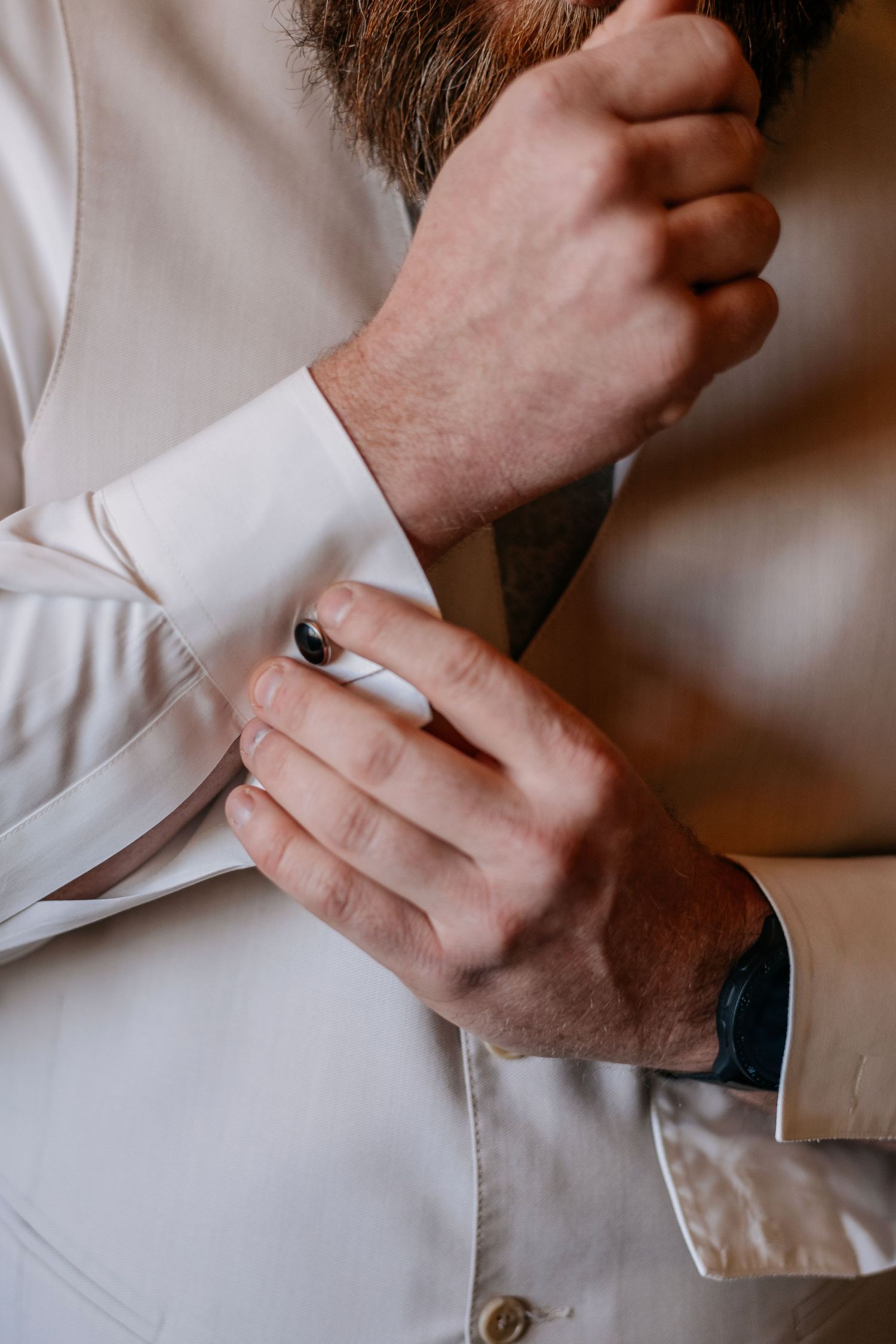 Groom fastening black cufflinks on white dress shirt sleeve before wedding ceremony.