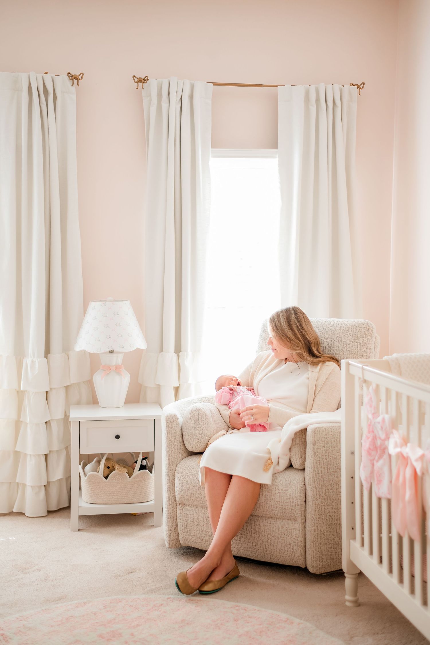 A serene nursery setting with ruffled curtains and a comfortable armchair by the window.