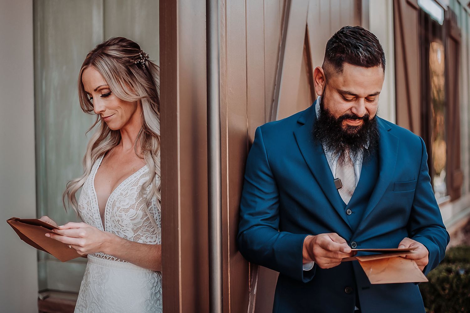 Bride in lace gown and groom in blue suit reading wedding vows separately before ceremony.