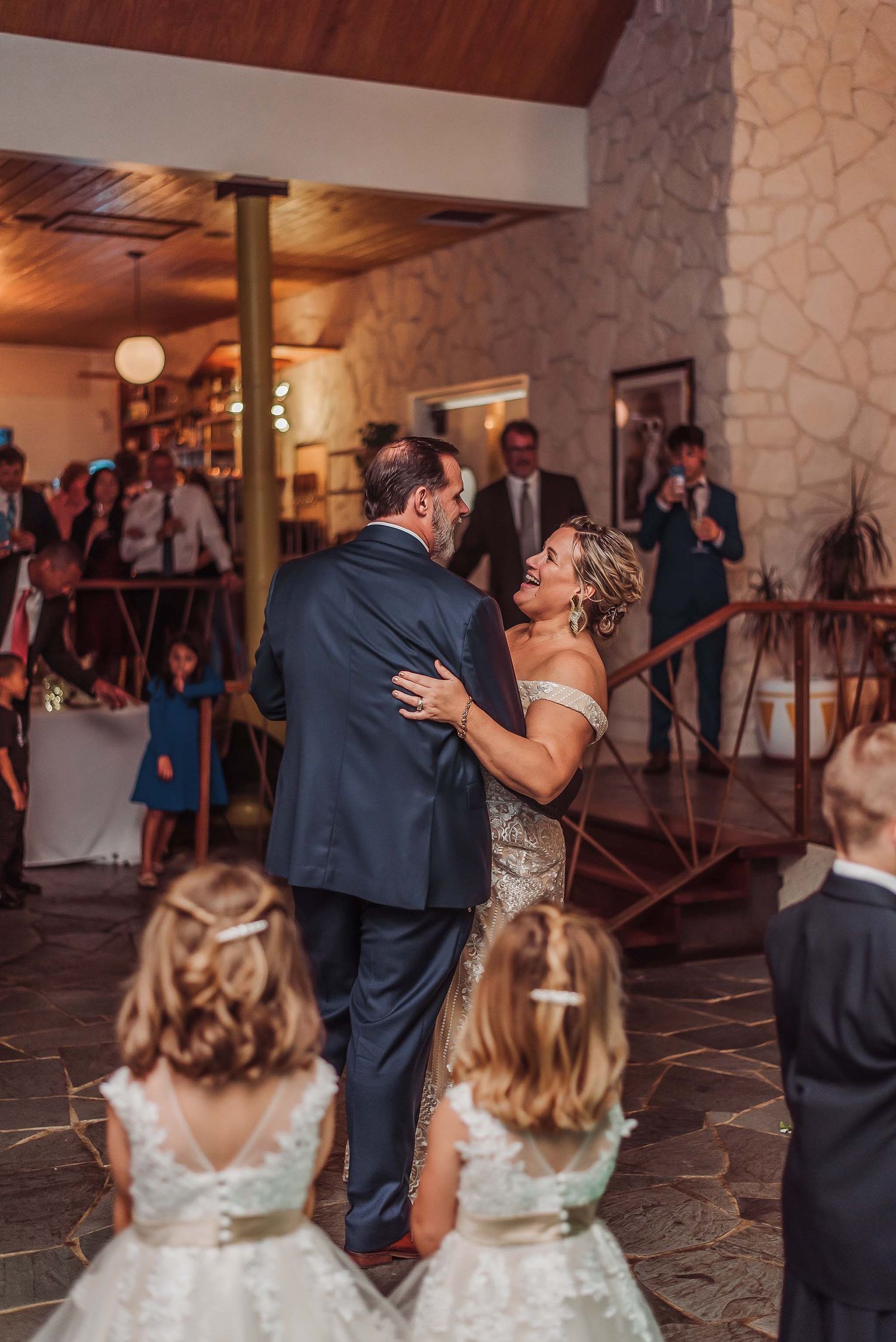 Bride and groom share their first dance at wedding reception while flower girls watch in foreground.