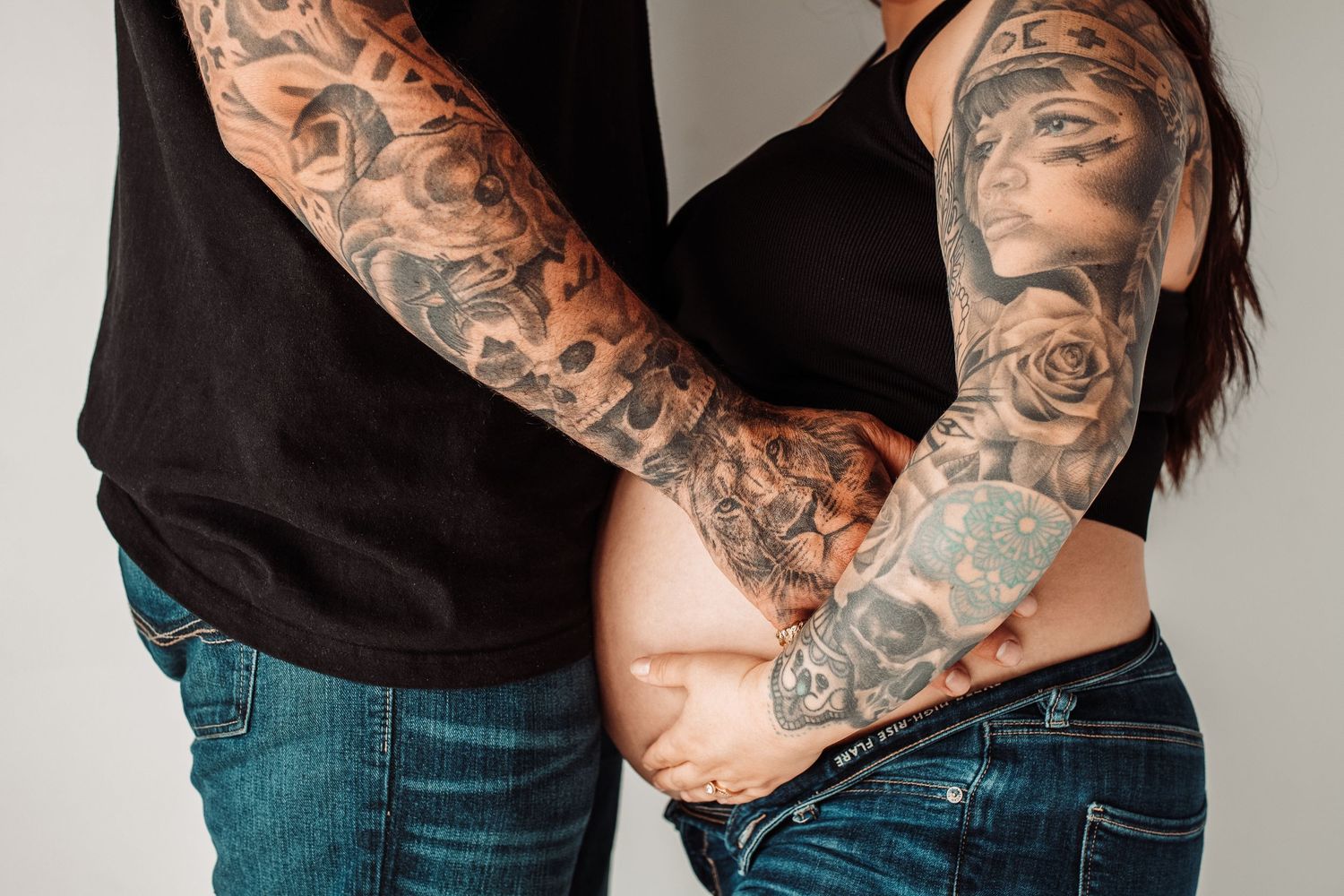 Close-up of tattooed arms embracing around a waist showing detailed black and gray sleeve artwork.