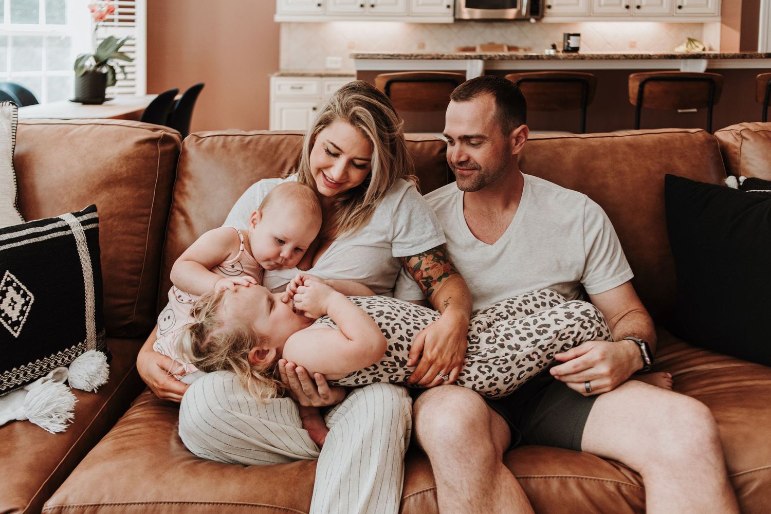 A family relaxes together on a cozy brown couch in a warmly lit living room setting.
