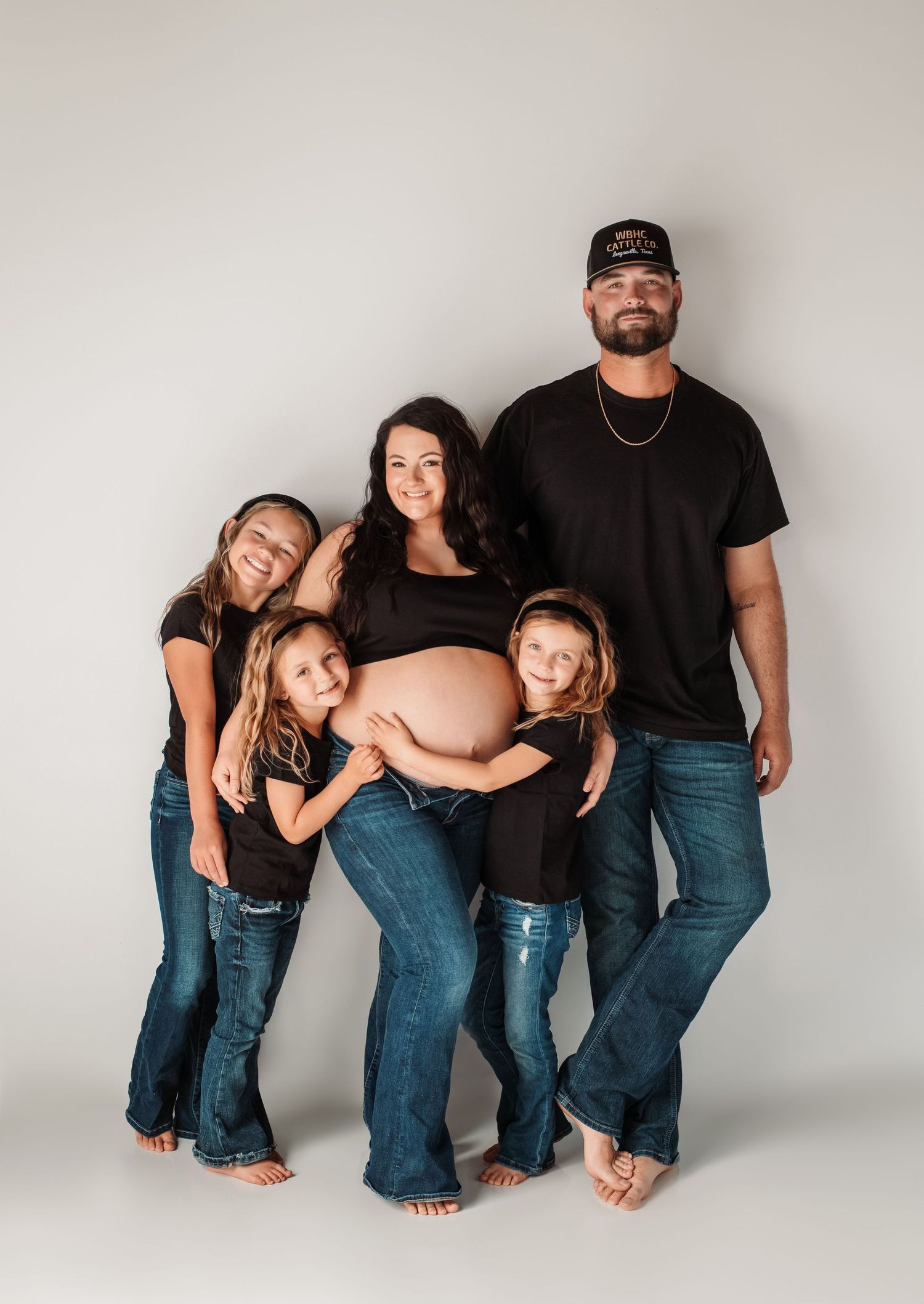 Family maternity photo with expecting mother and family members in casual denim against grey background.