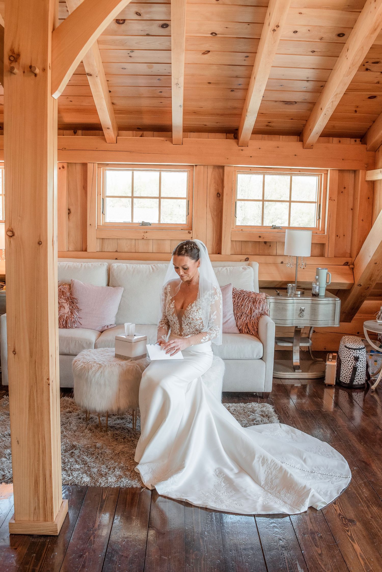 Bride in lace wedding dress reads letter while seated in rustic wooden cabin bridal suite.