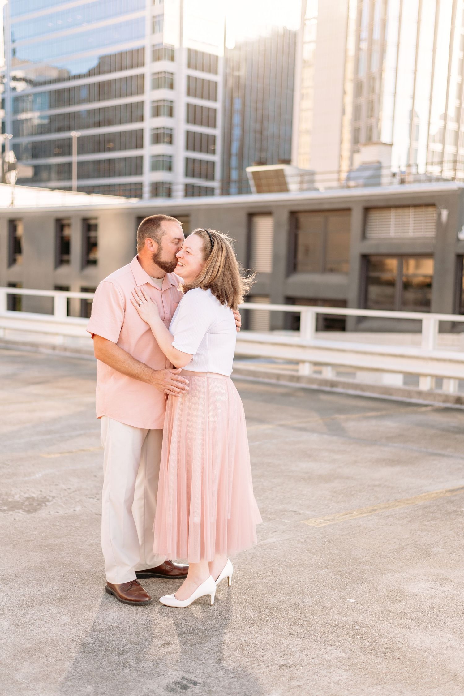 Romantic couple embracing in coordinated pink and white outfits on a modern rooftop setting.