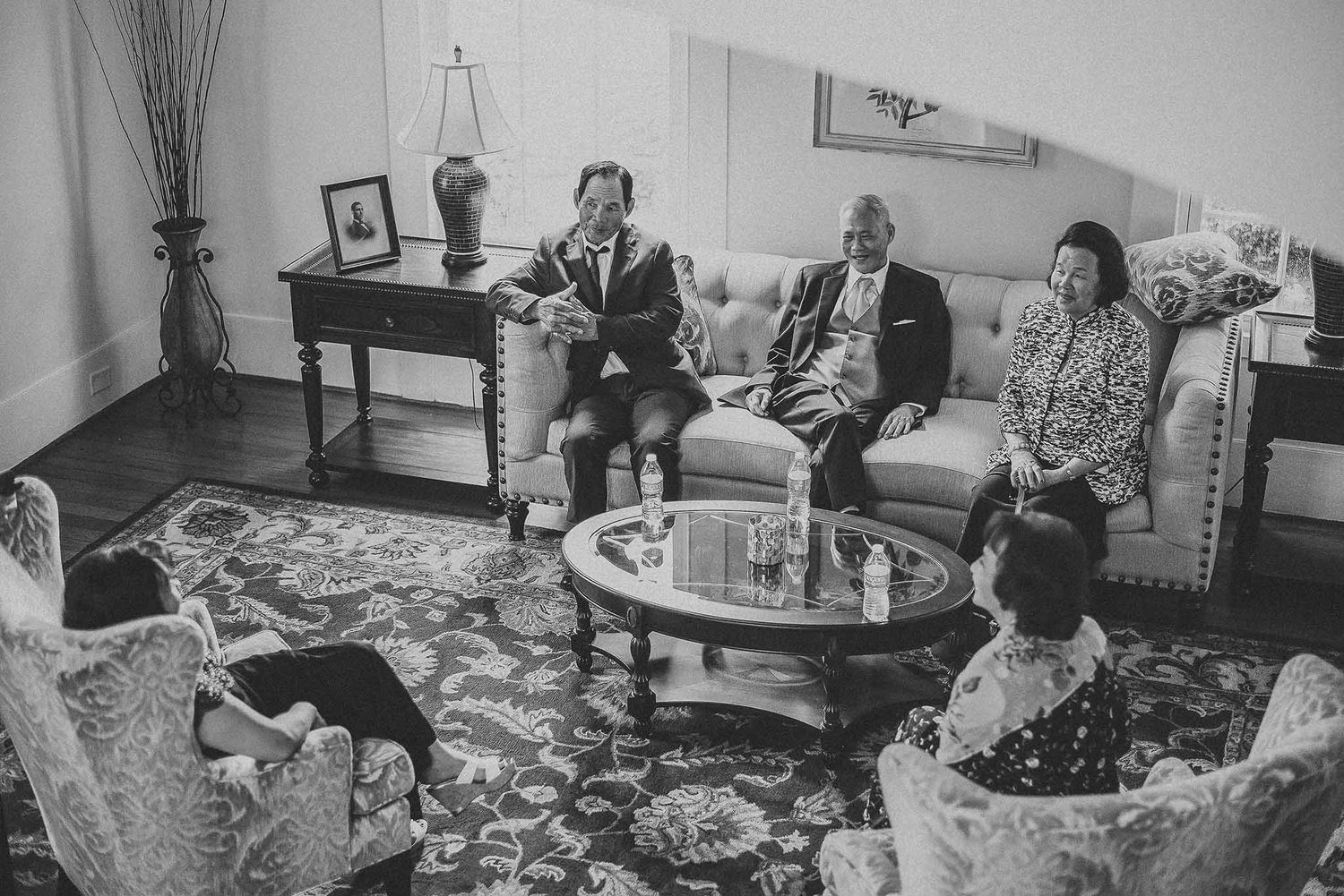 Black and white photo of a family gathering in an elegant living room with ornate rug and antique furniture.